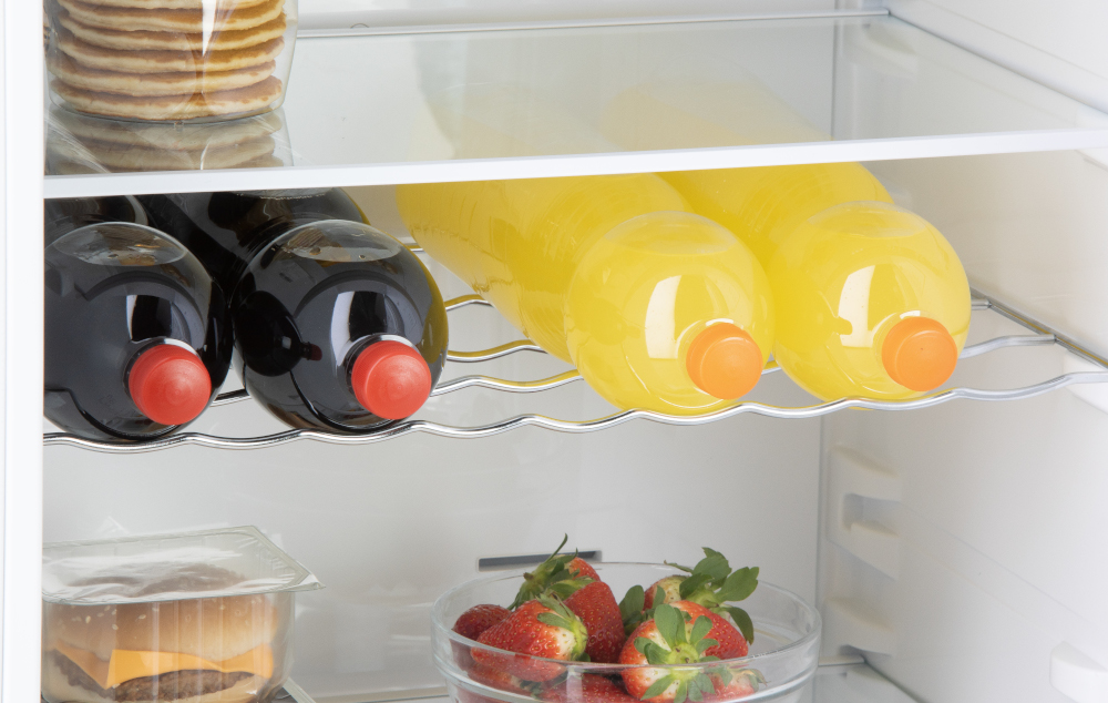 Refrigerator shelf with juice bottles, dark bottles, and a bowl of strawberries.