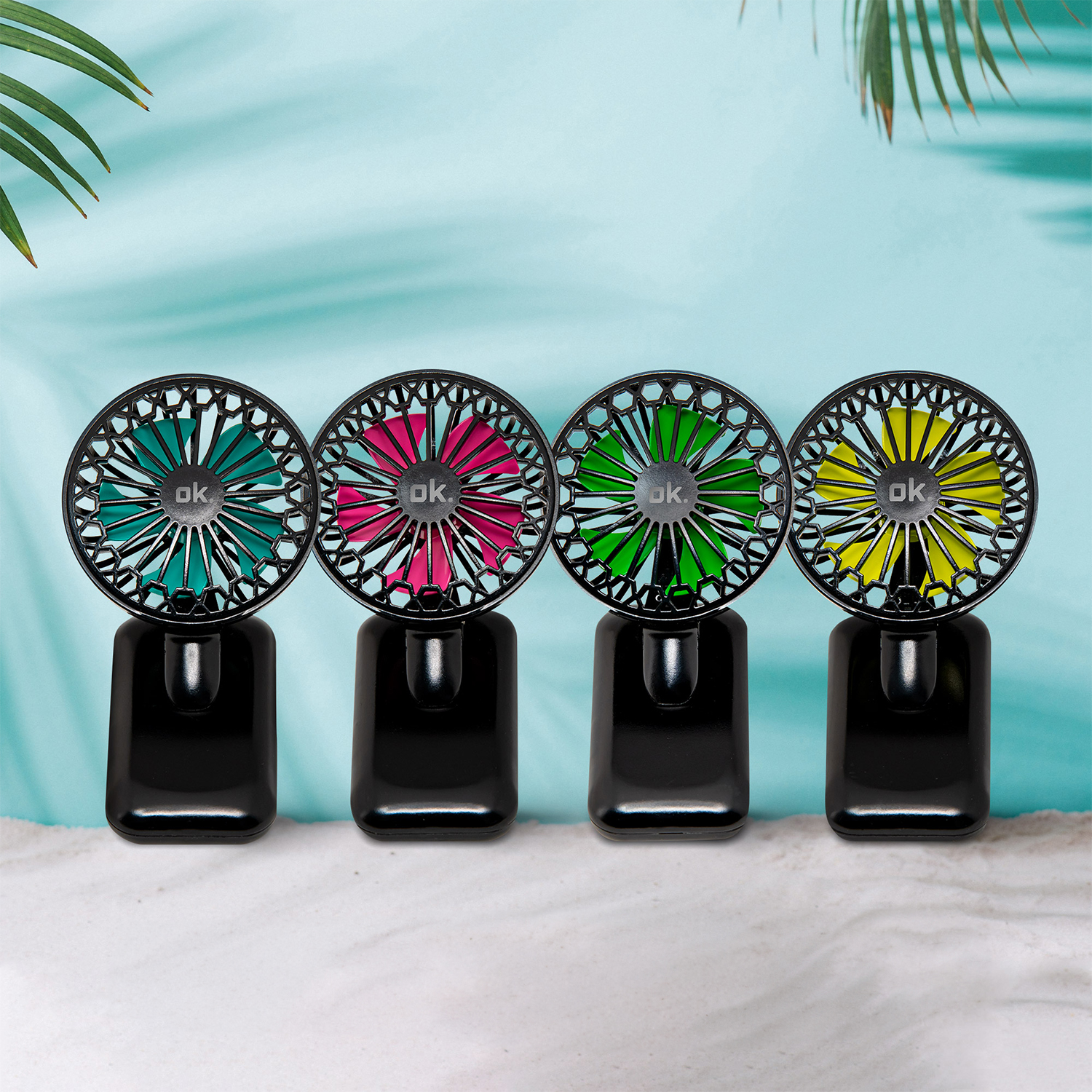 Quattro mini ventilatori neri con pale di diversi colori. Sono su una superficie sabbiosa con sfondo blu.
