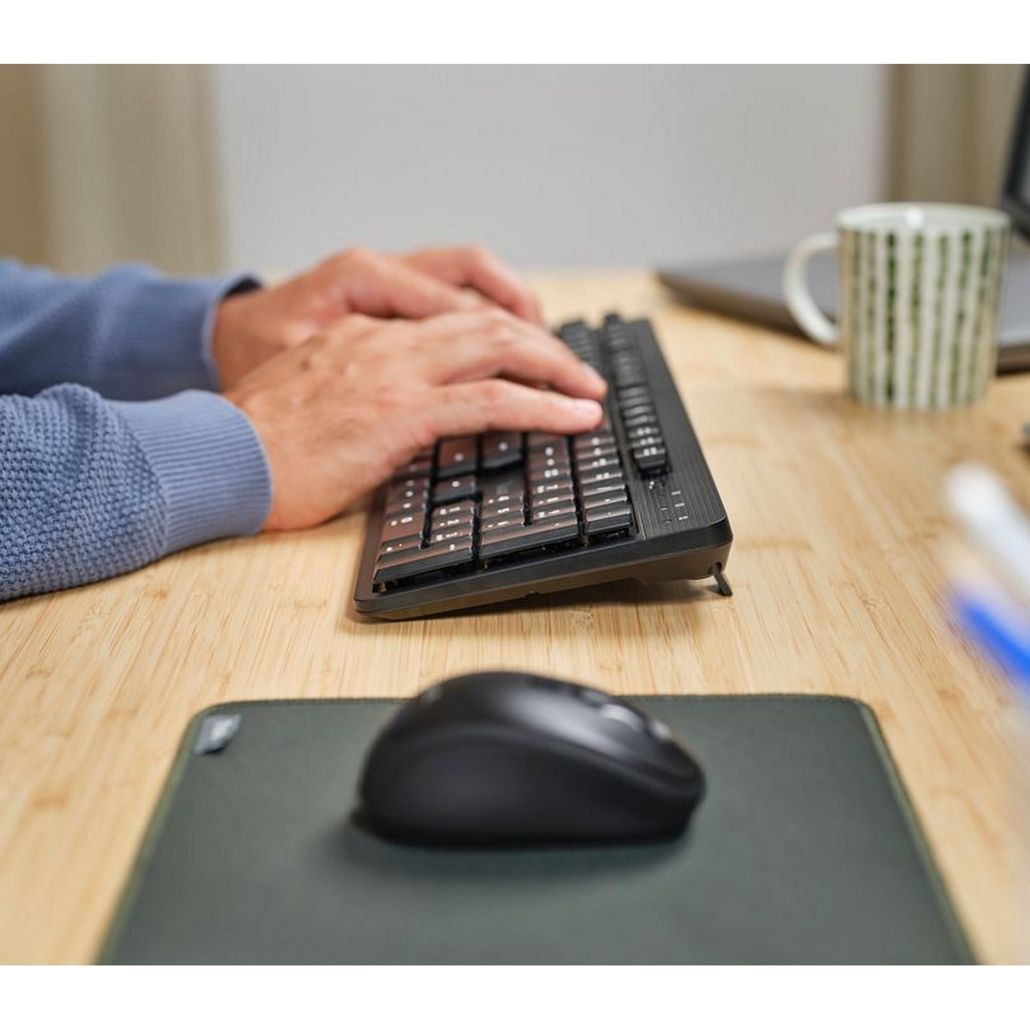 Hands typing on black keyboard on wooden desk, mouse visible.