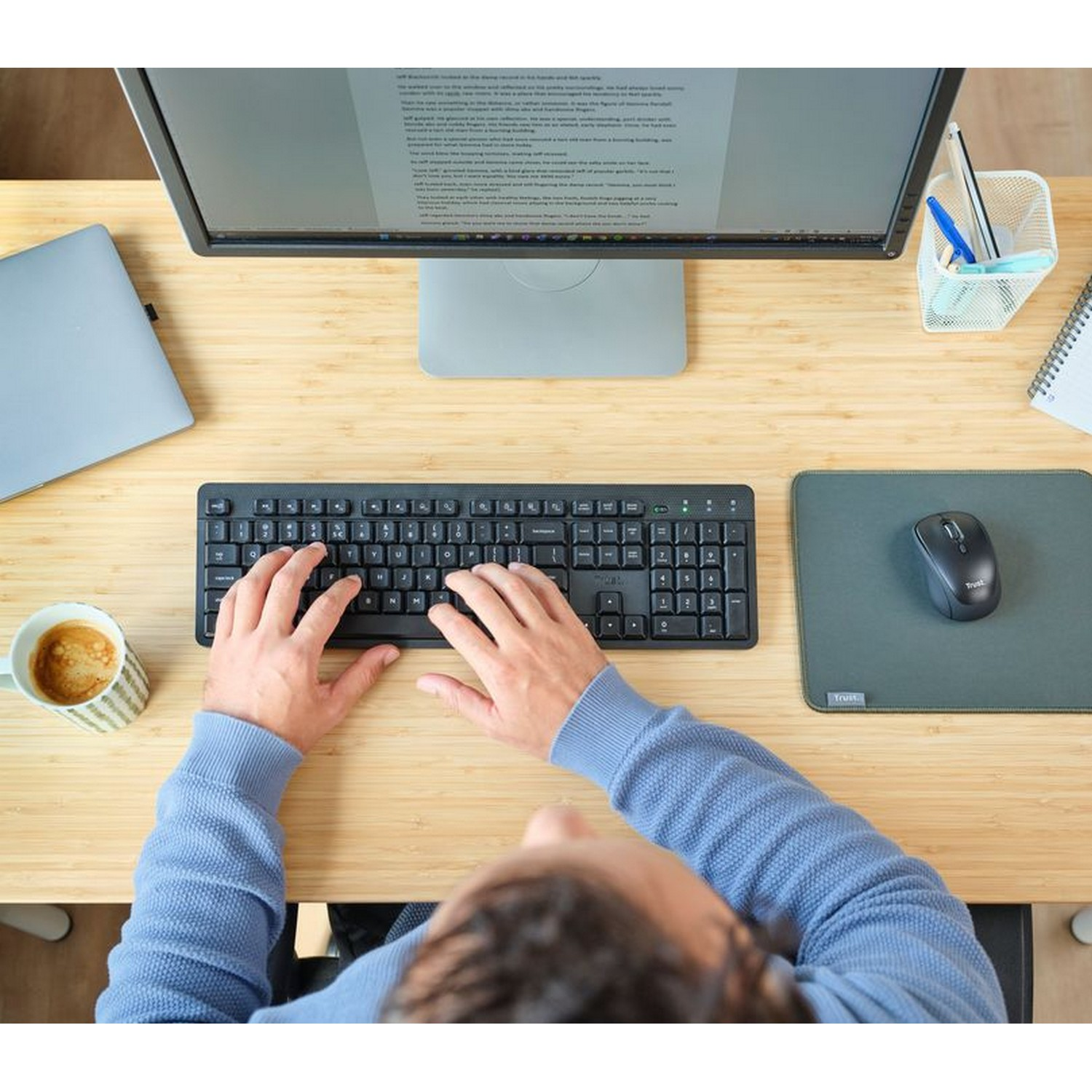 Overhead view of a person typing on a keyboard with a monitor, mouse, and coffee cup on a desk.