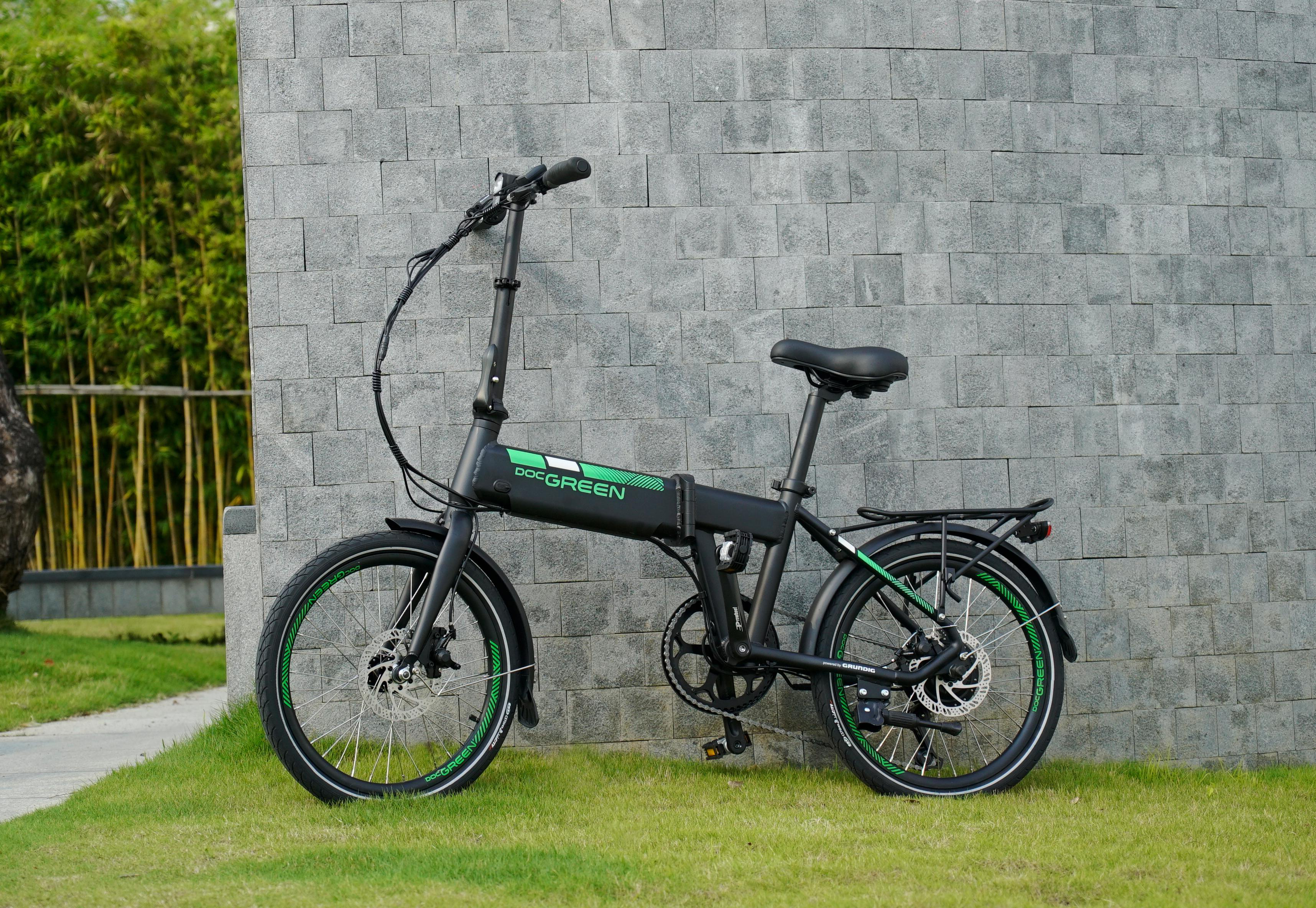 Schwarzes Elektrofahrrad steht an grauer Wand. Grüne Details sind sichtbar.
