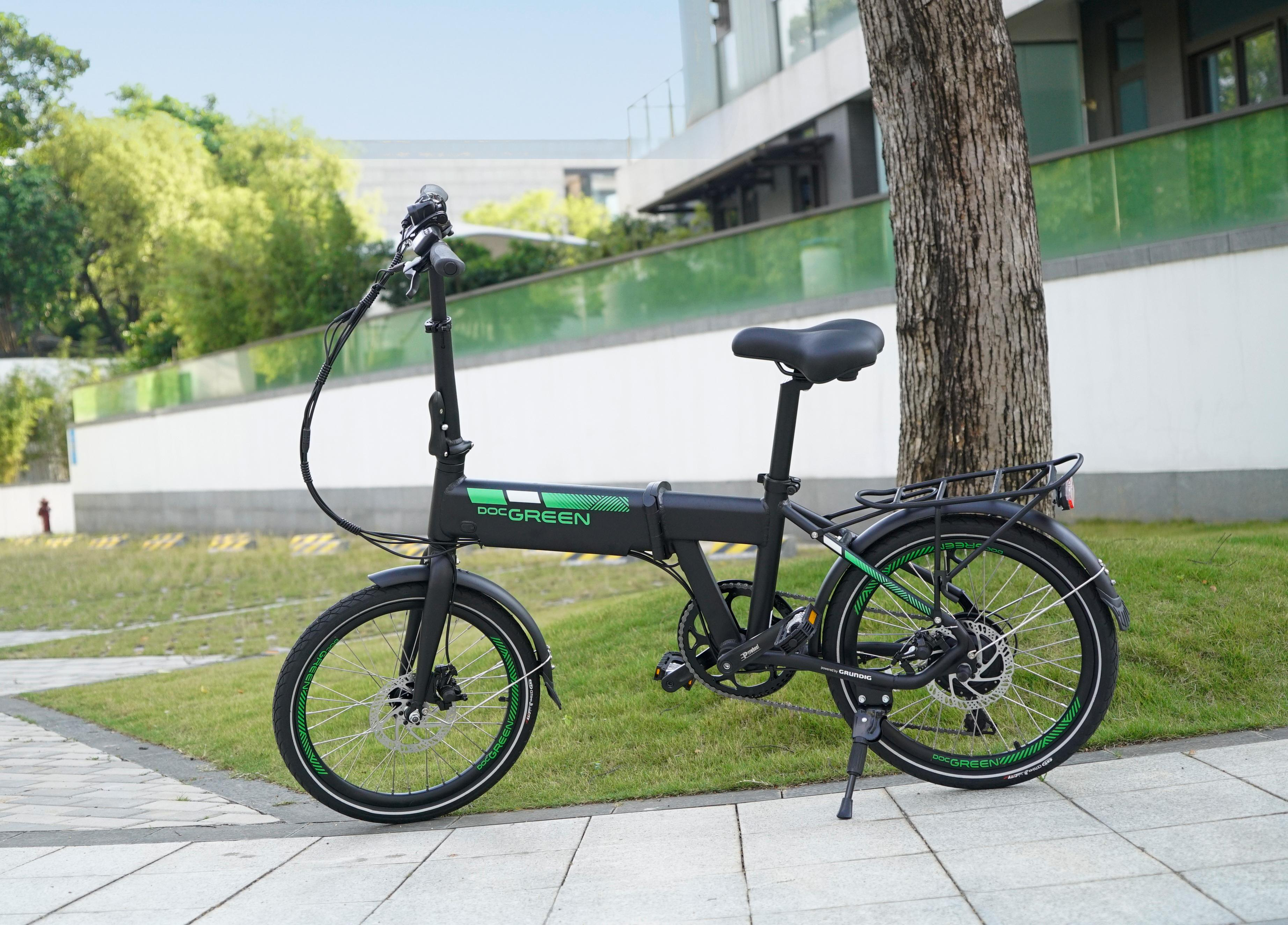 Ein Elektrofahrrad. Es ist schwarz mit grünen Akzenten. Es steht auf einem Bürgersteig neben einem Baum.