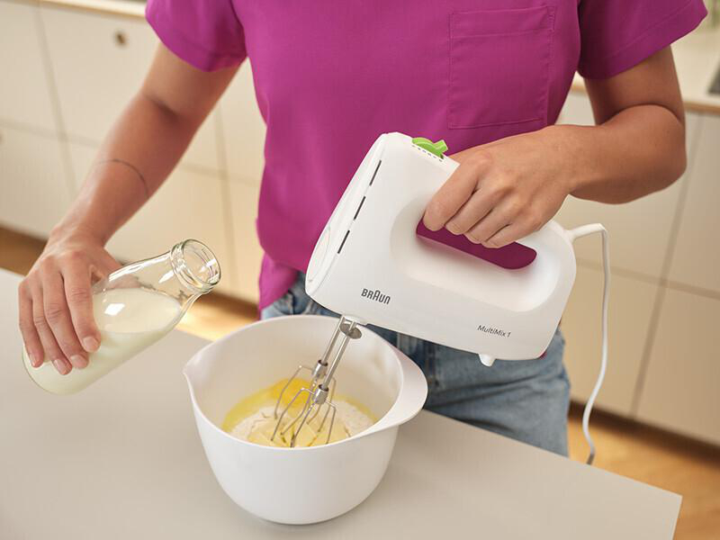 Person gießt Flüssigkeit aus einer Glasflasche in eine Schüssel mit Handmixer.