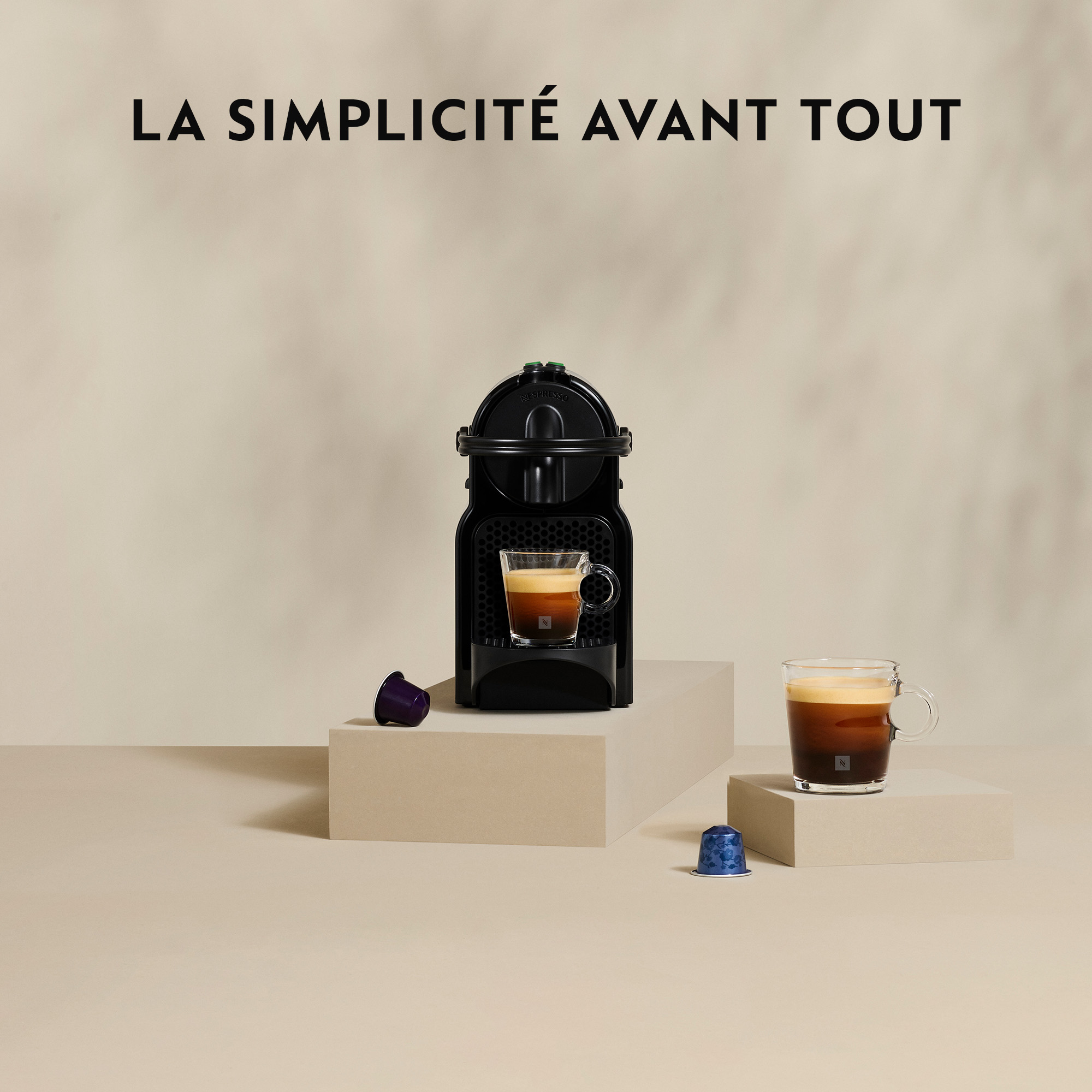 Une machine Nespresso noire avec une tasse de café, des capsules et le texte 'LA SIMPLICITÉ AVANT TOUT'.
