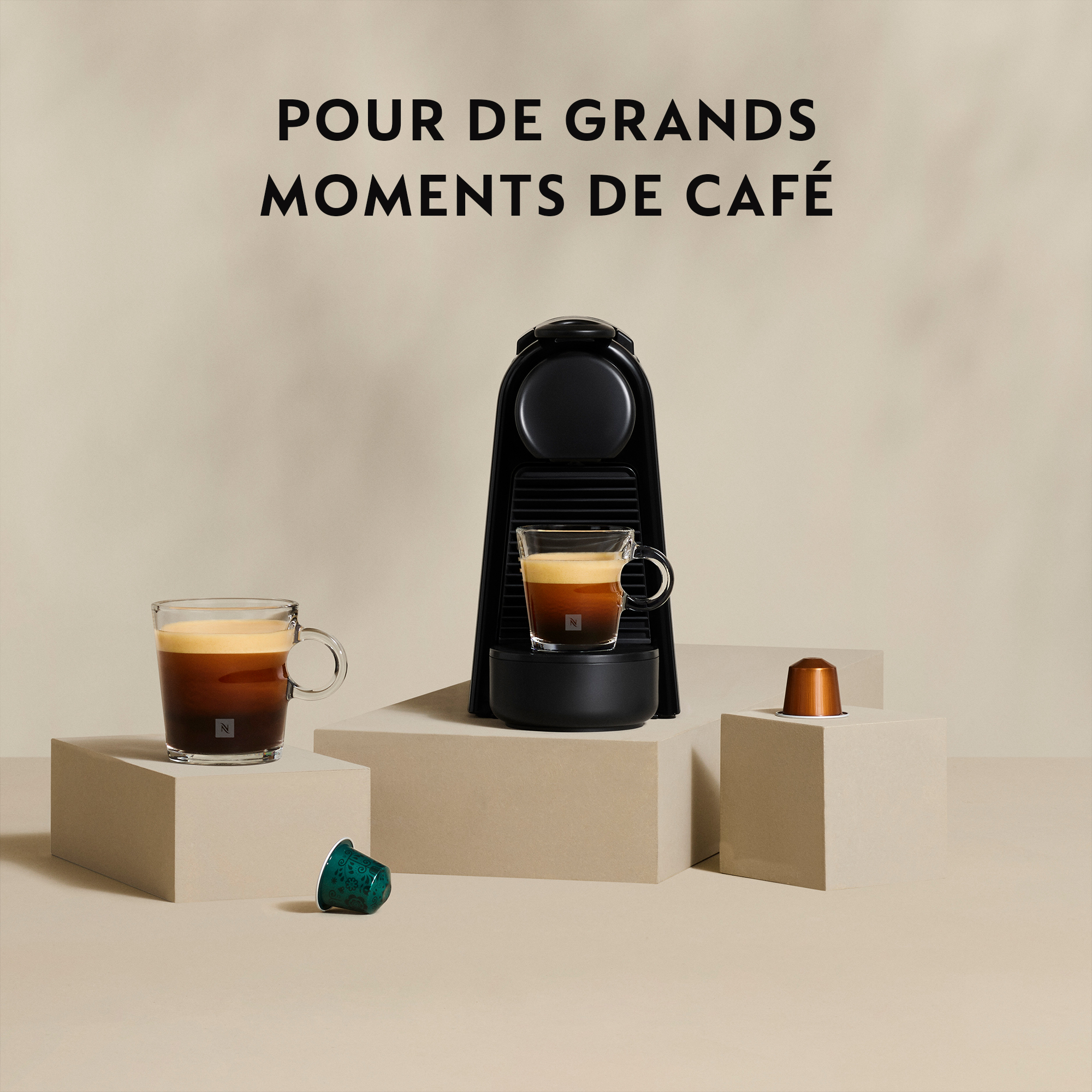 Machine à expresso noire avec deux tasses de café et capsules. Texte : Pour de grands moments de café.