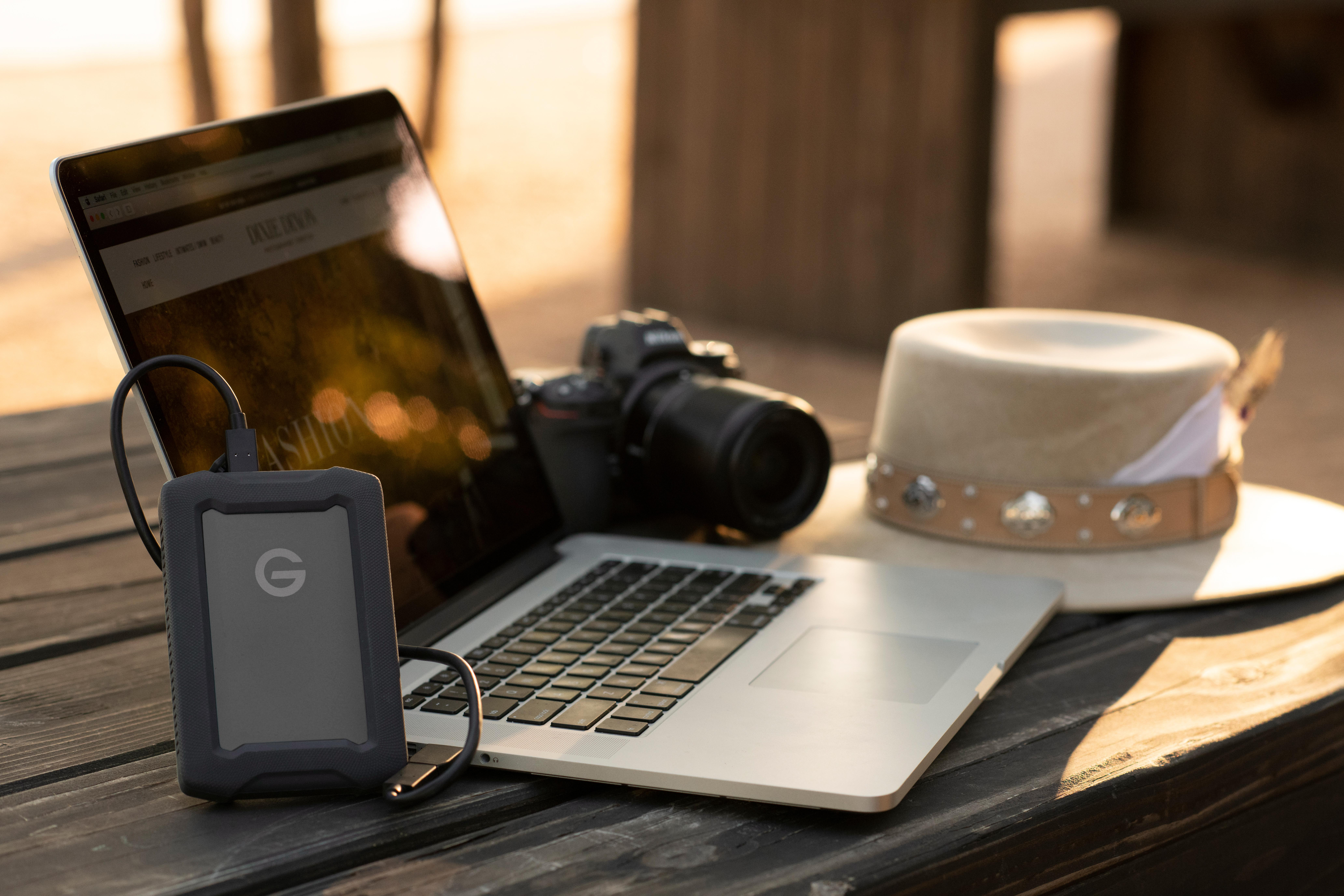 Laptop, Kamera, externe Festplatte und Hut auf Holzoberfläche.