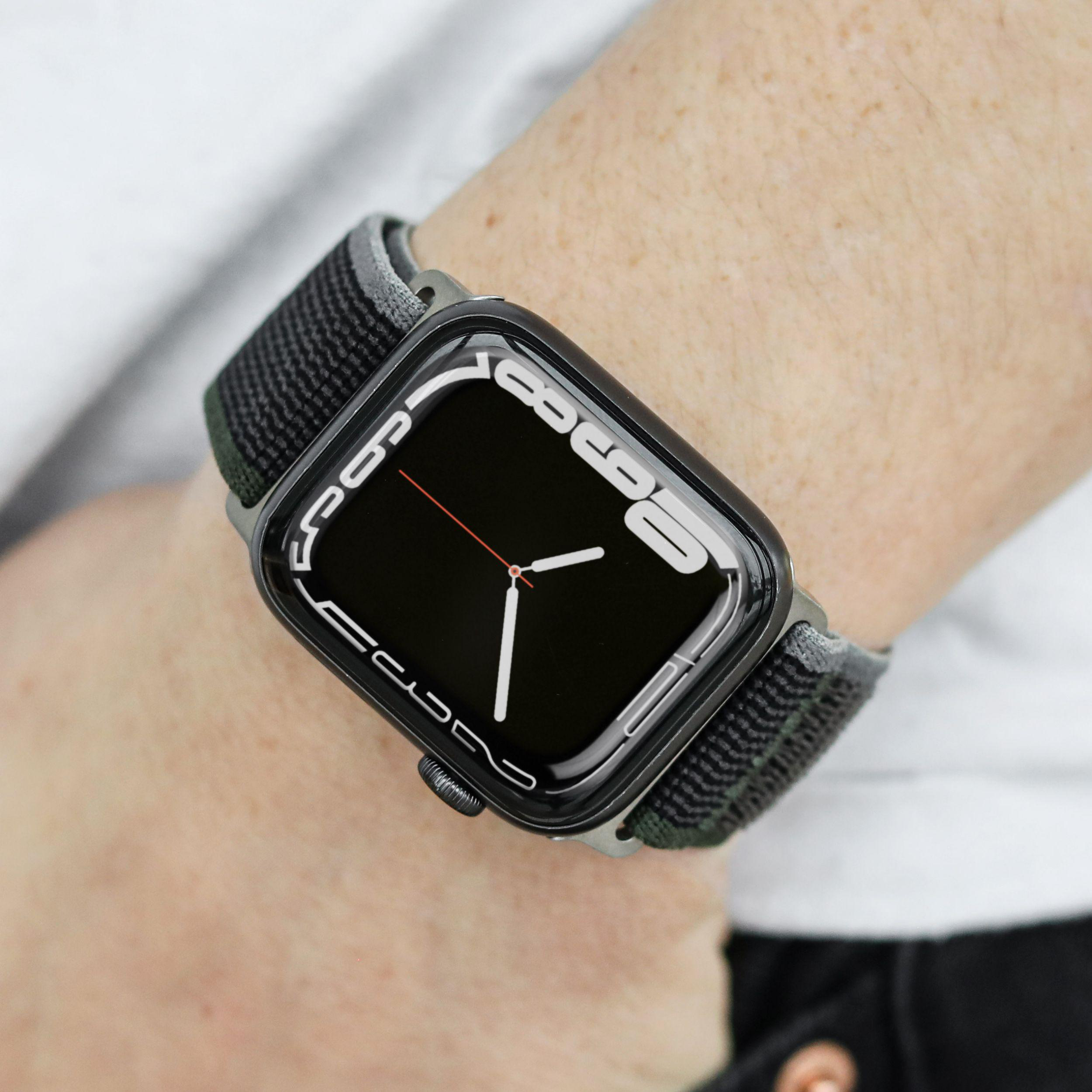 Apple Watch am Handgelenk, schwarzer Bildschirm mit Uhrzeit, olivgrünes Armband.