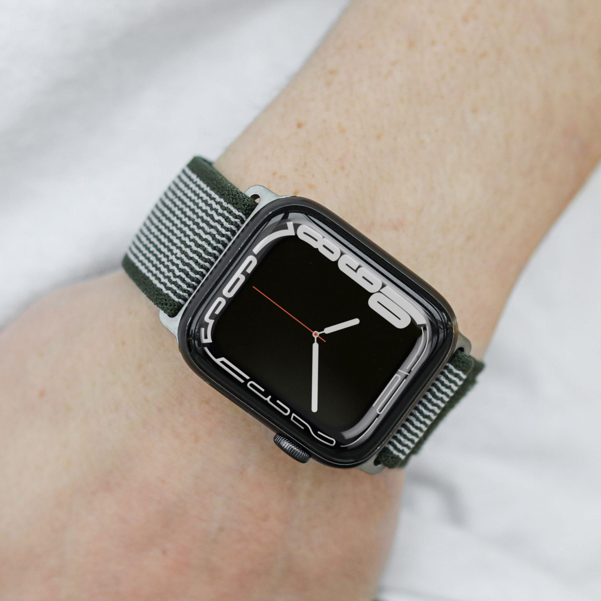 Handgelenk mit Smartwatch. Die Uhr hat ein schwarzes Display mit weißen Zeigern und ein grün gestreiftes Band.