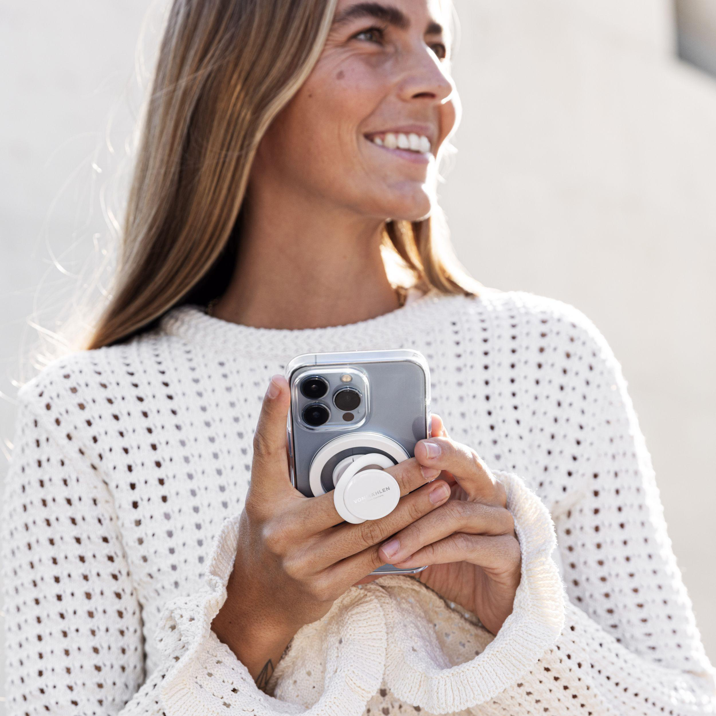 Frau hält Telefon mit weißem PopSocket vor weißer Wand.