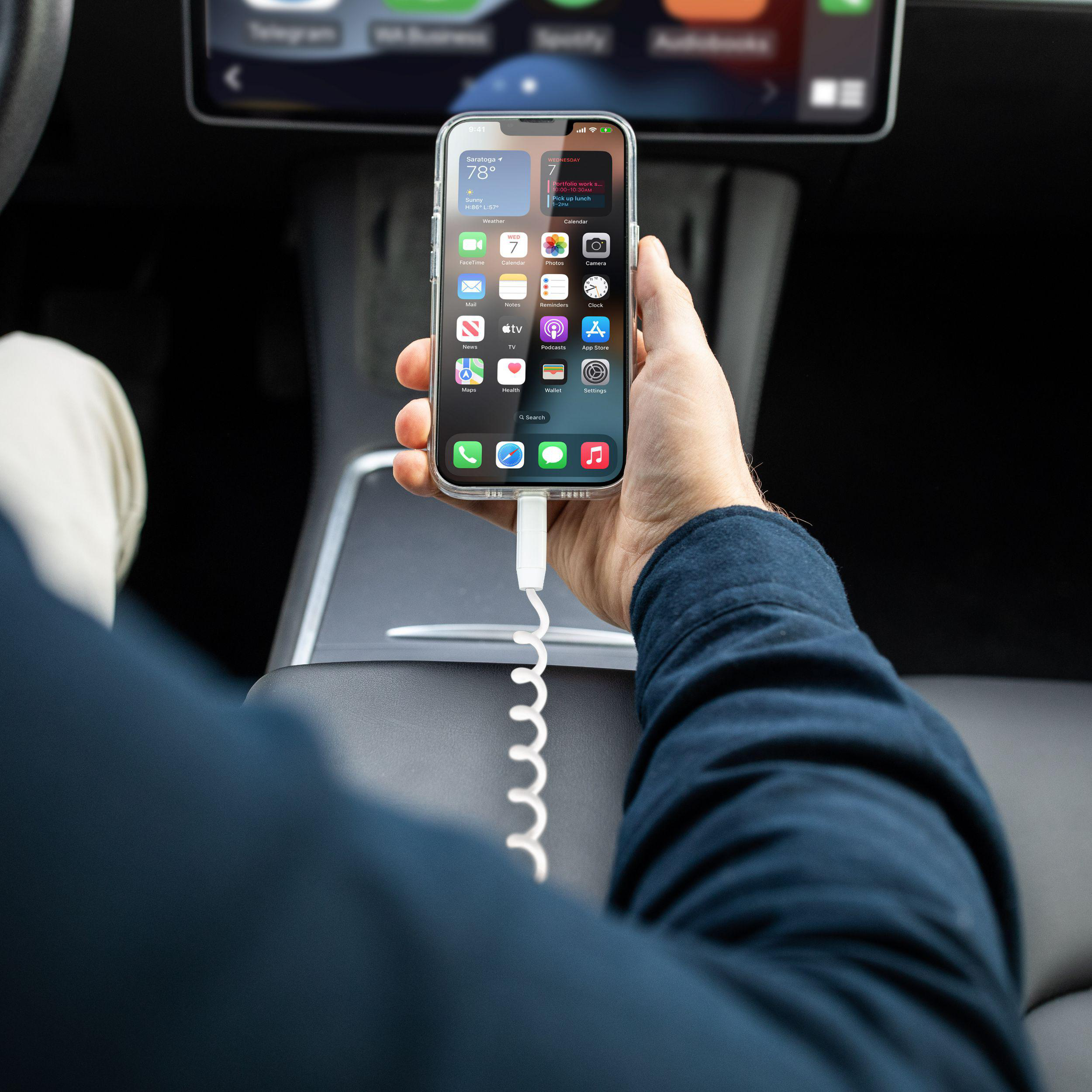 Eine Person hält ein Telefon in einem Auto, das mit einem Ladekabel verbunden ist und ein Autodisplay zeigt.