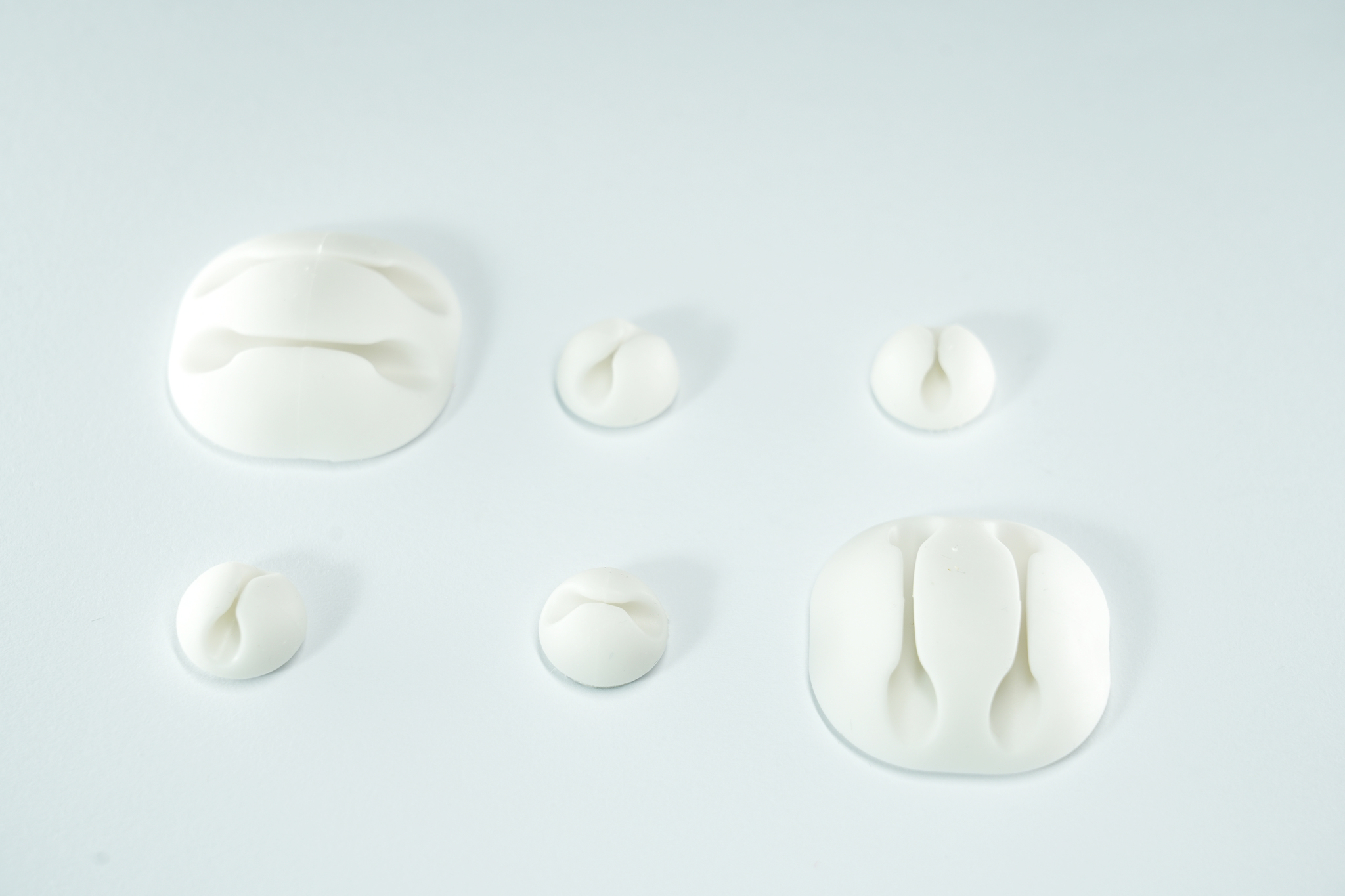 Organisateurs de câbles blancs, de tailles et formes variées, sur une surface blanche. Pour la gestion des câbles.