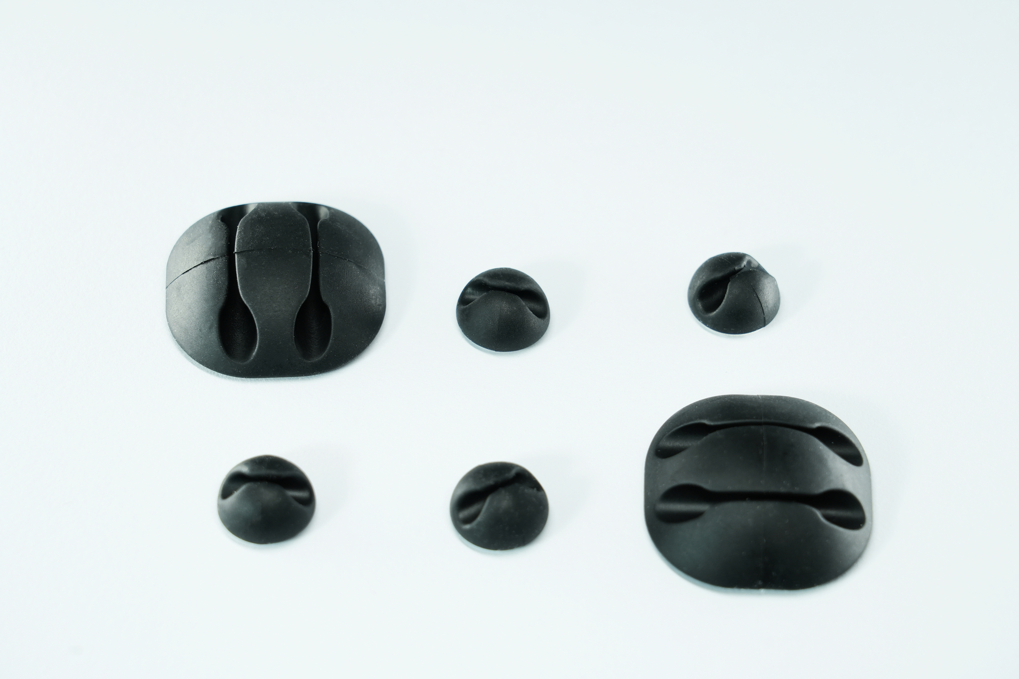 Attaches de câble noires de différentes tailles, disposées sur une surface blanche. Certaines sont fermées, d'autres ouvertes.