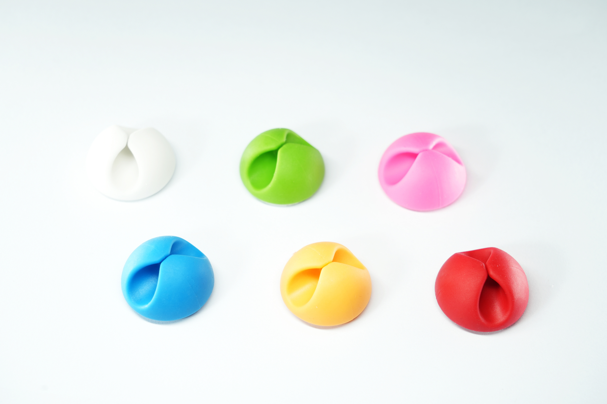 Sei organizzatori di cavi in vari colori su una superficie bianca.