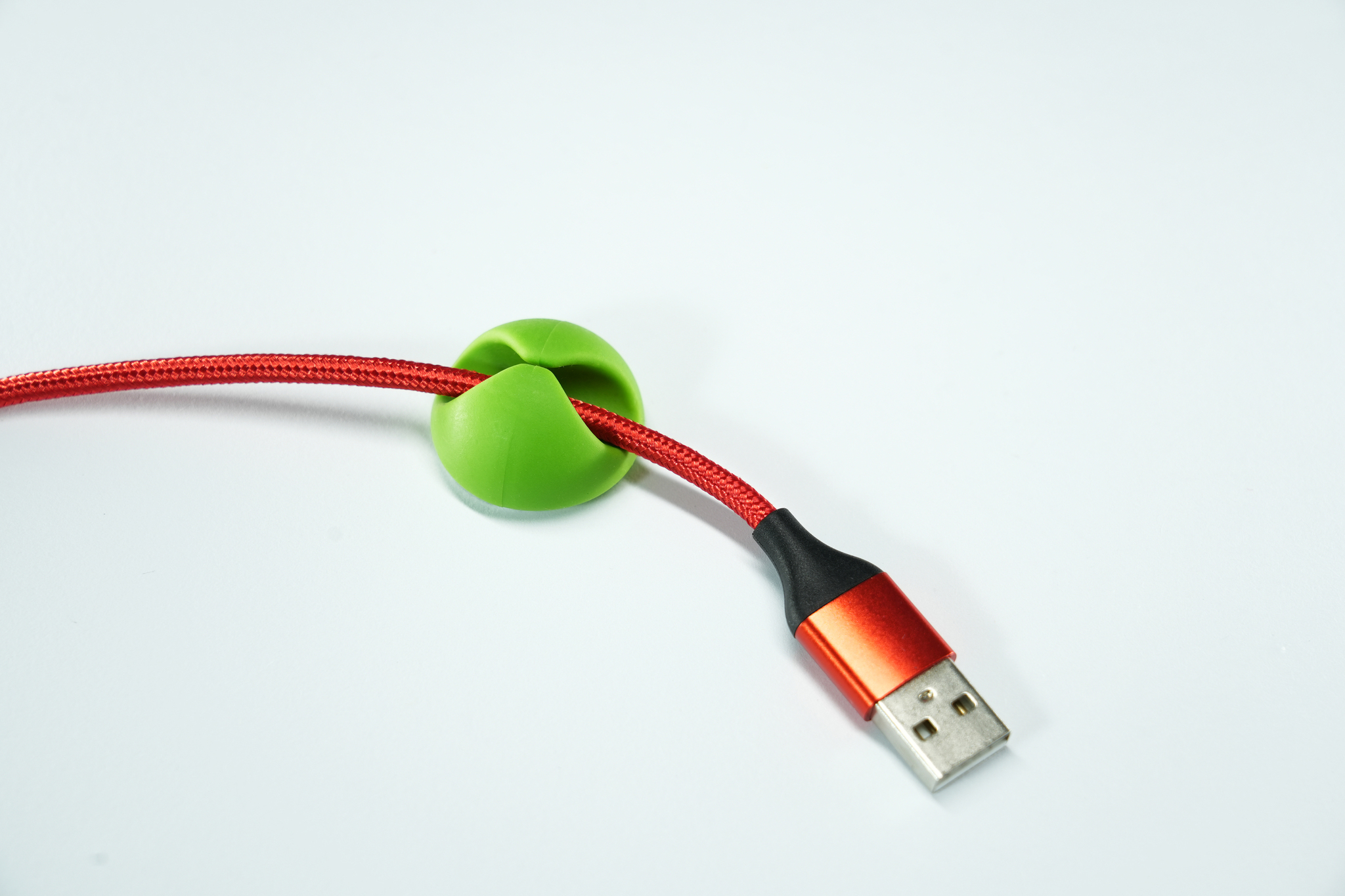 Un fermacavo verde che tiene un cavo rosso con un connettore USB. È su una superficie bianca.