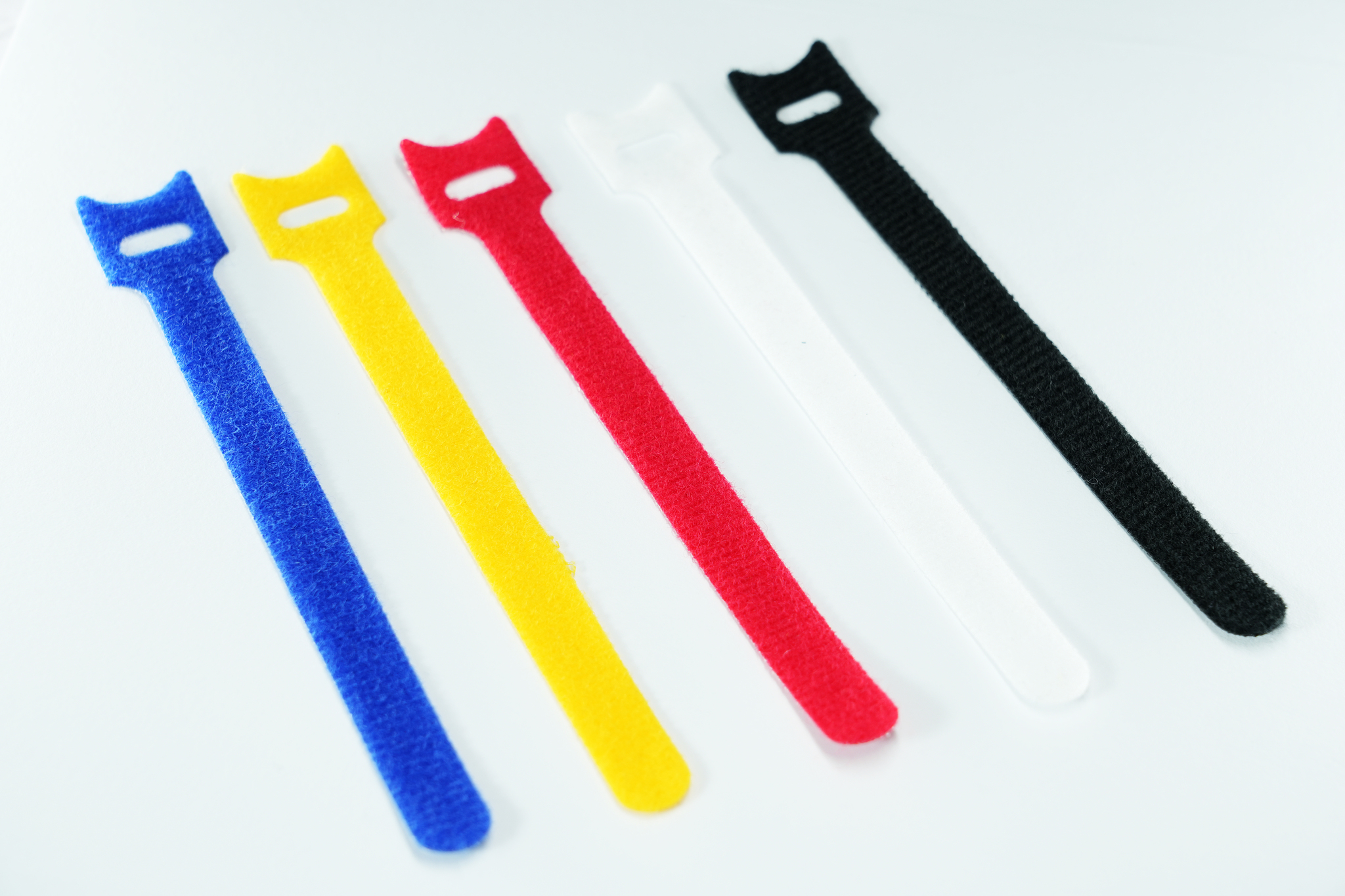 Cinq colliers de serrage colorés sur une surface blanche. Bleu, jaune, rouge, blanc et noir.