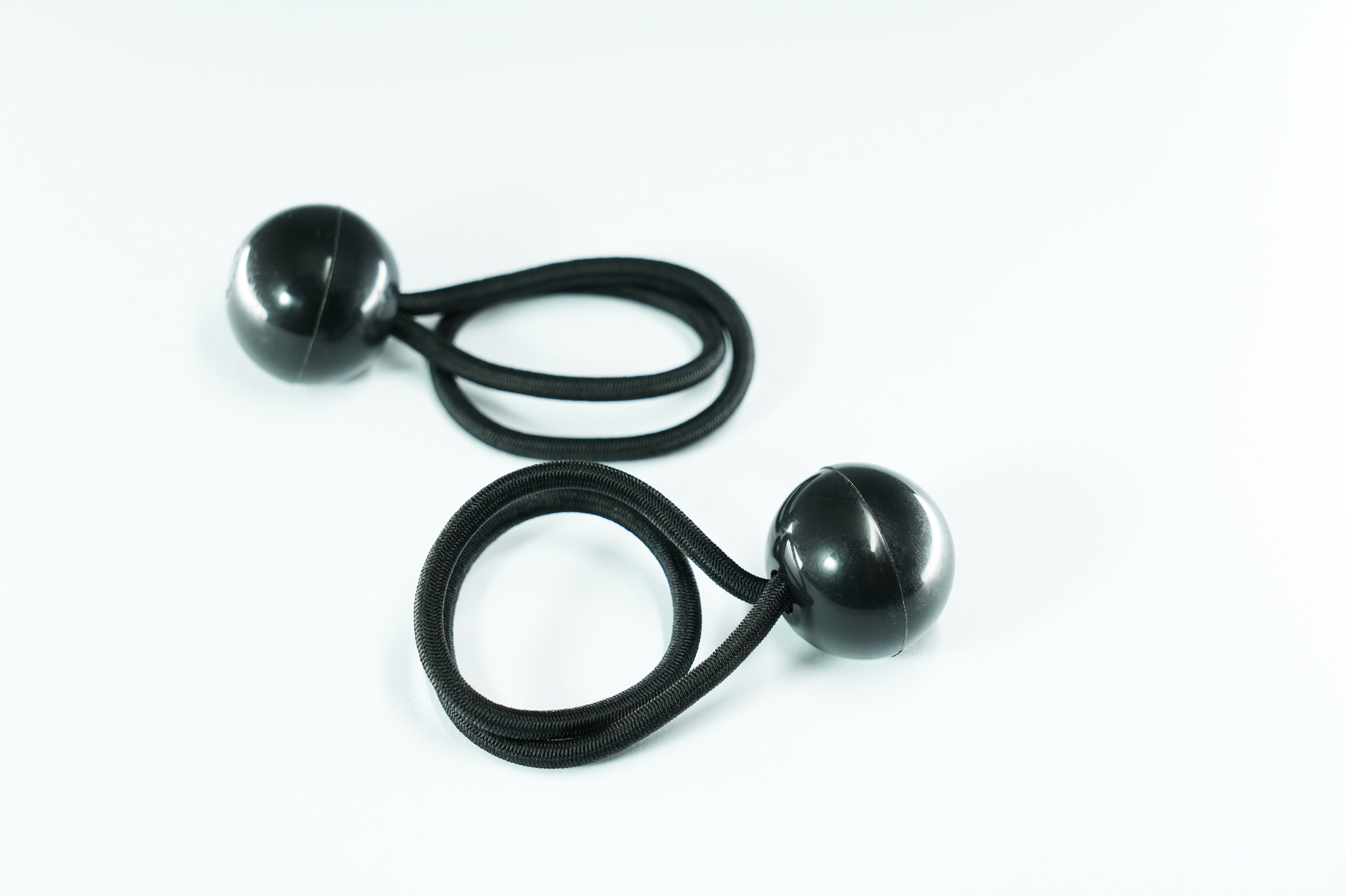 Deux tendeurs élastiques noirs avec boules noires à chaque extrémité, sur surface blanche.