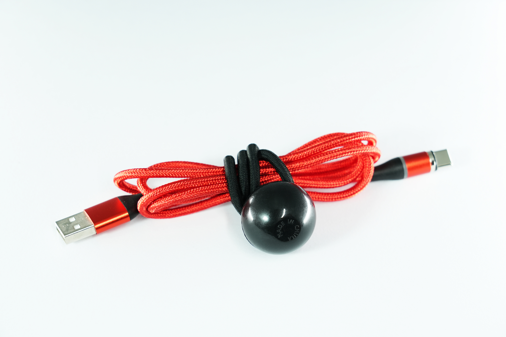 Câble rouge avec boule noire attachée, USB et un autre connecteur visible. Le tout sur fond blanc.