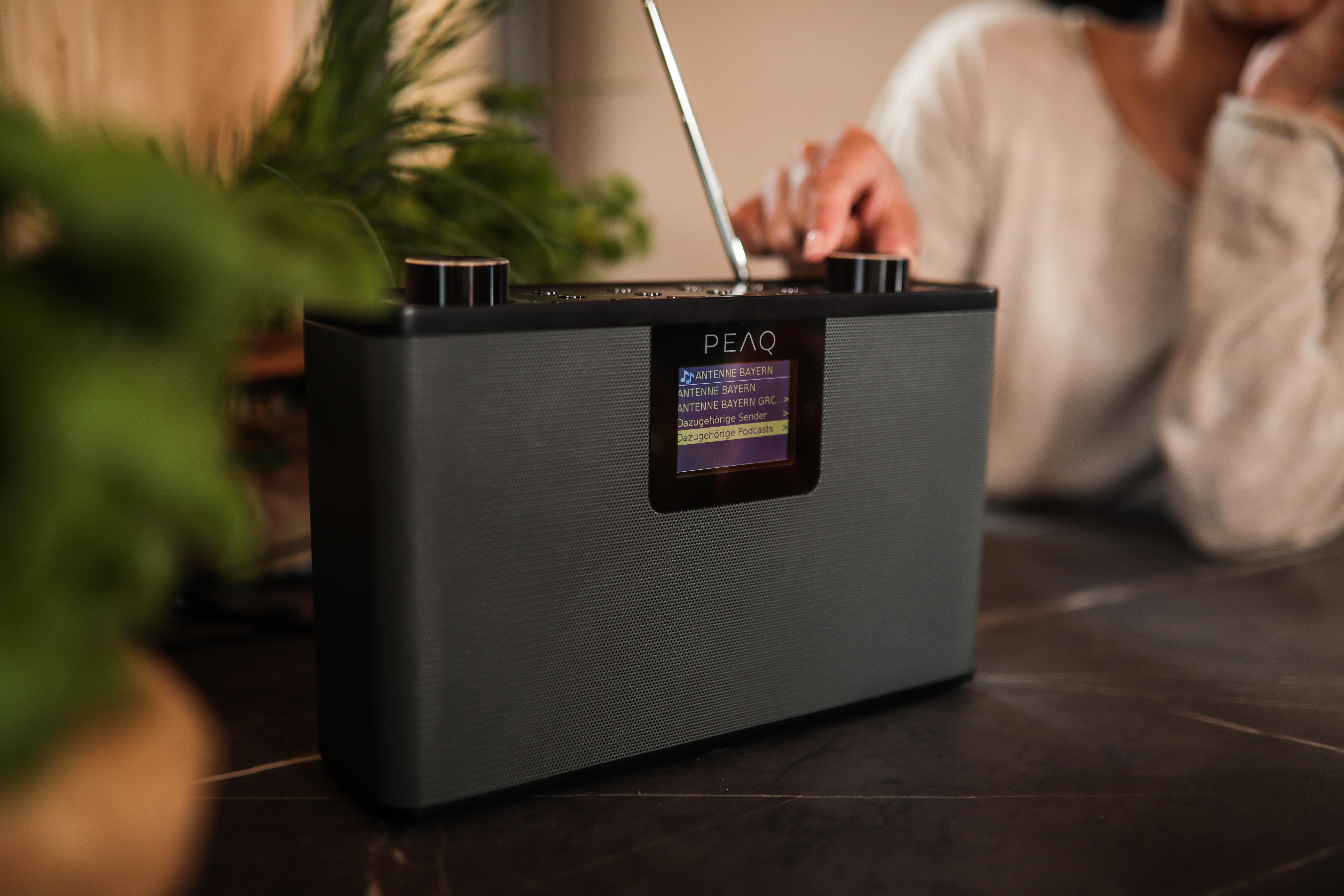 Ein schwarz-graues Radio mit kleinem Bildschirm, Hand einer Person am Knopf.