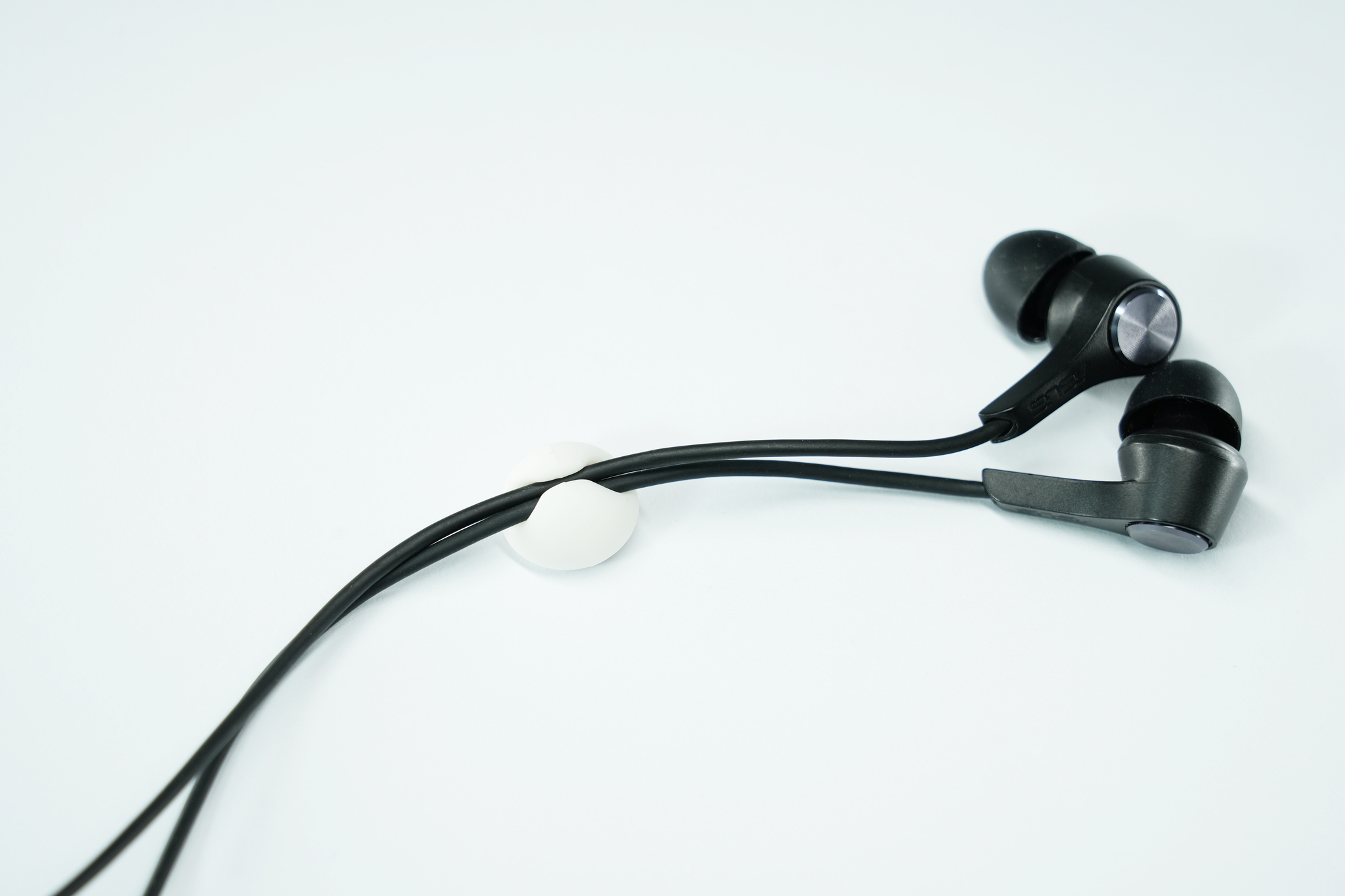 Auricolari con cavi neri e una clip bianca su sfondo azzurro.