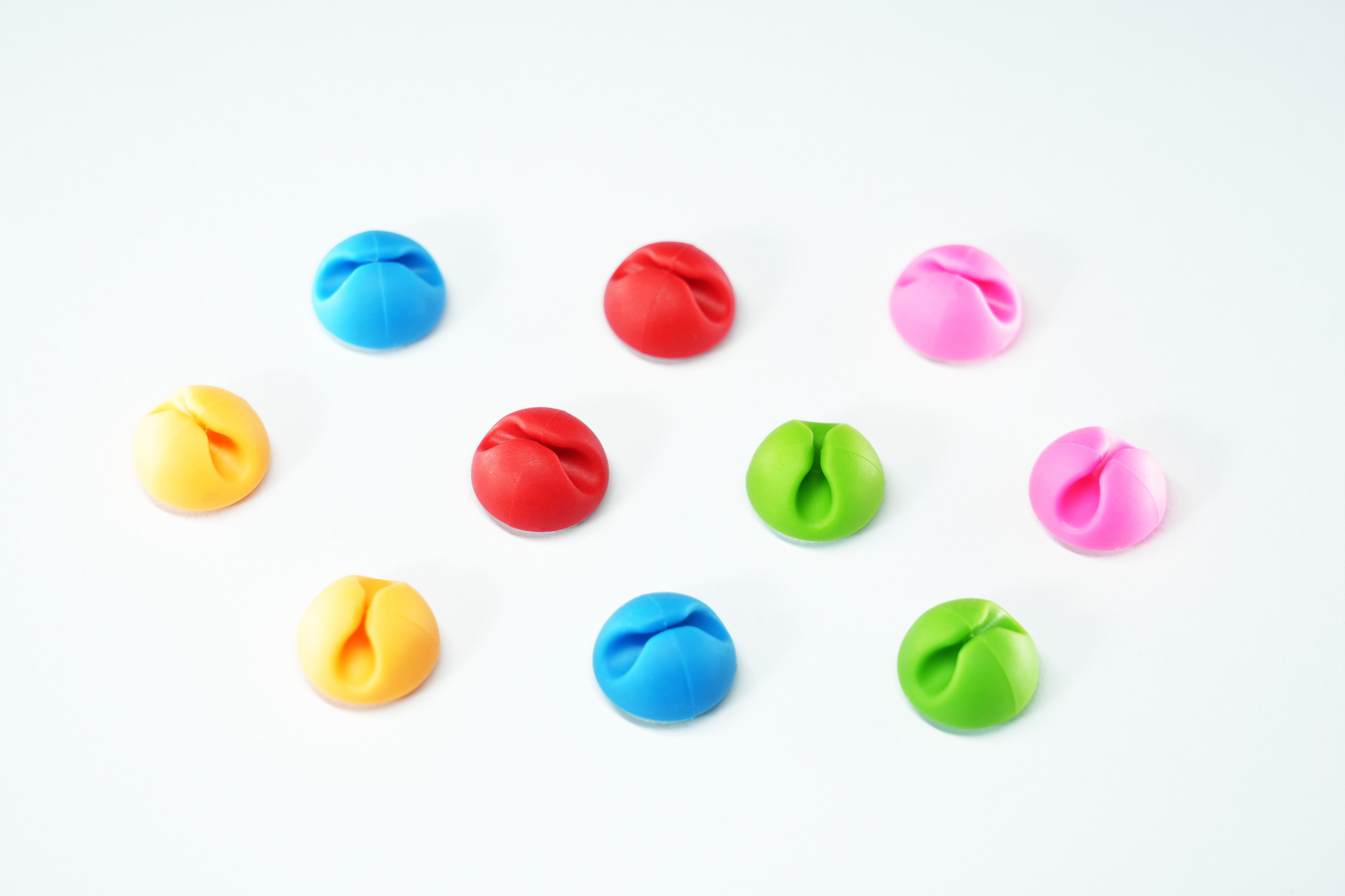 Dieci organizzatori di cavi multicolori su una superficie bianca: blu, rosso, verde, rosa, giallo.