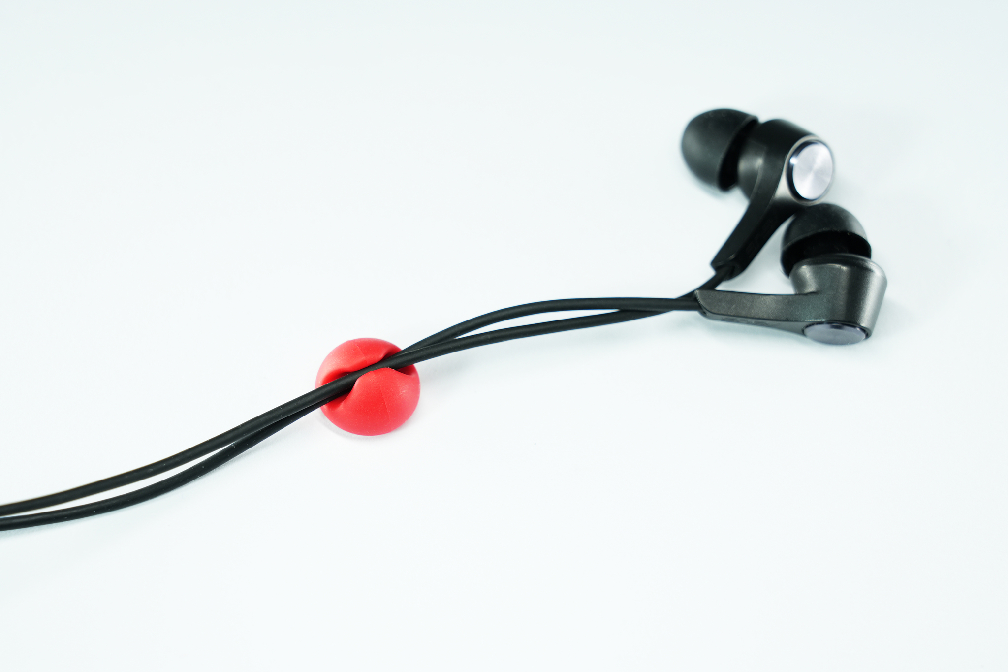 Auricolari neri con un organizer per cavi rosso su sfondo bianco.