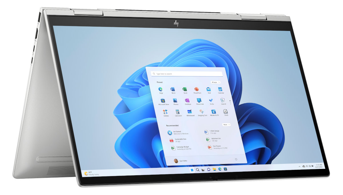 Otwarty srebrny laptop z interfejsem Windows 11 i niebieskim kwiatowym tłem.