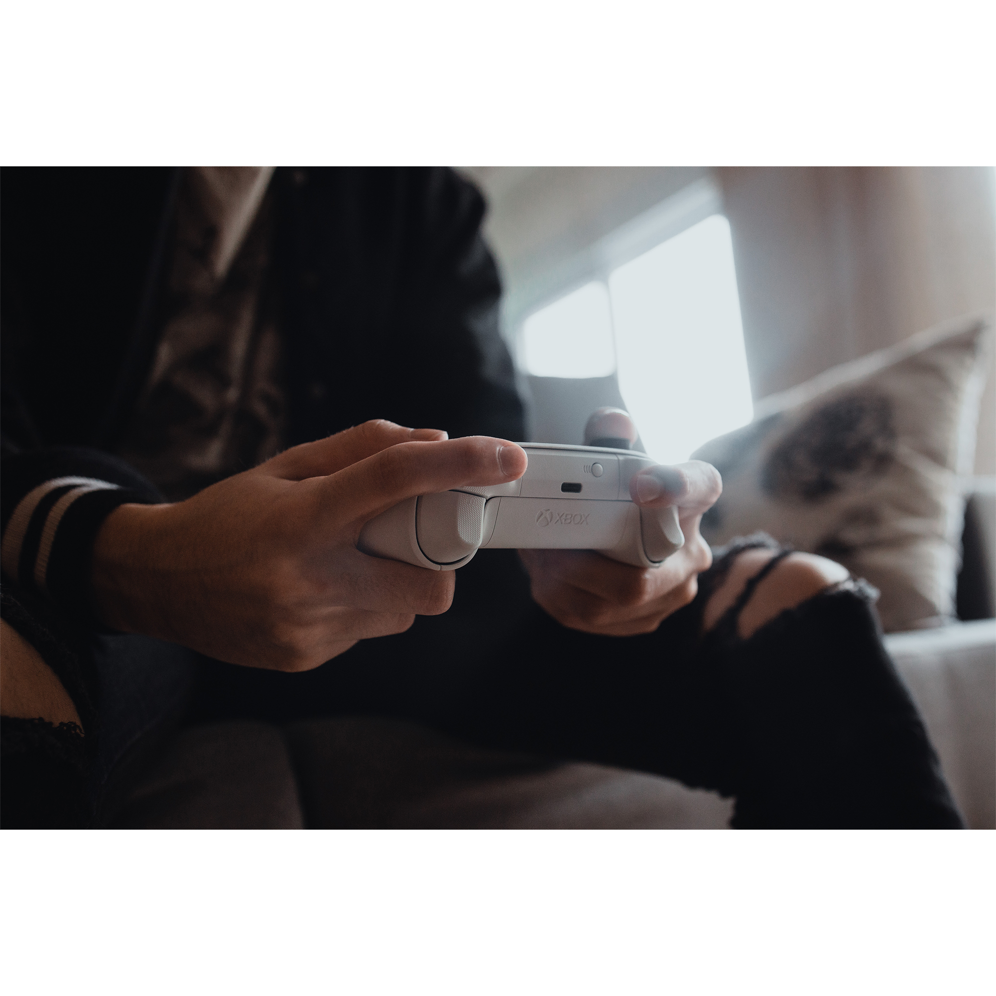 Una persona sostiene un mando blanco de Xbox, jugando un juego. La escena tiene iluminación suave.