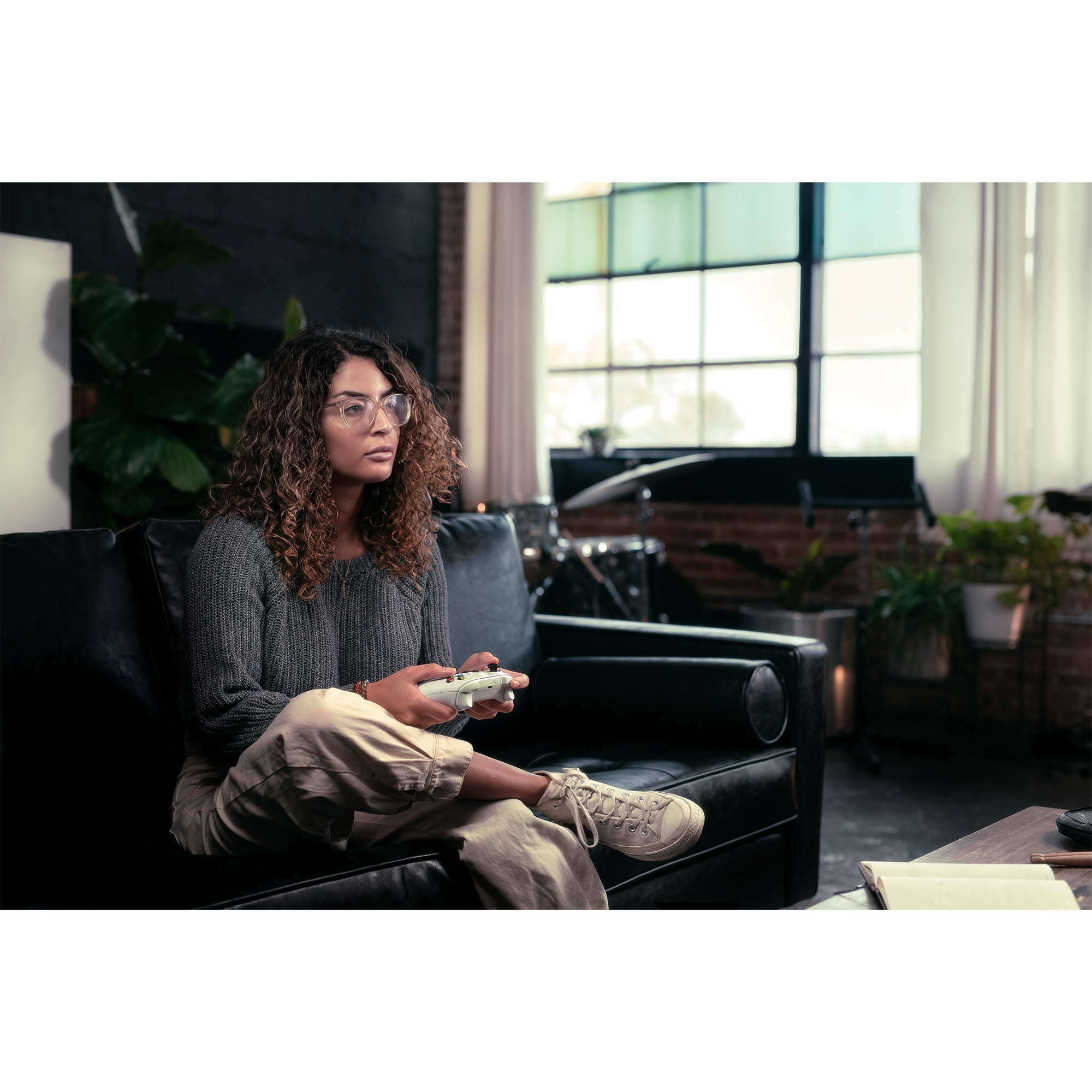 Mujer con gafas juega videojuegos. Está en un sofá negro, con mando.
