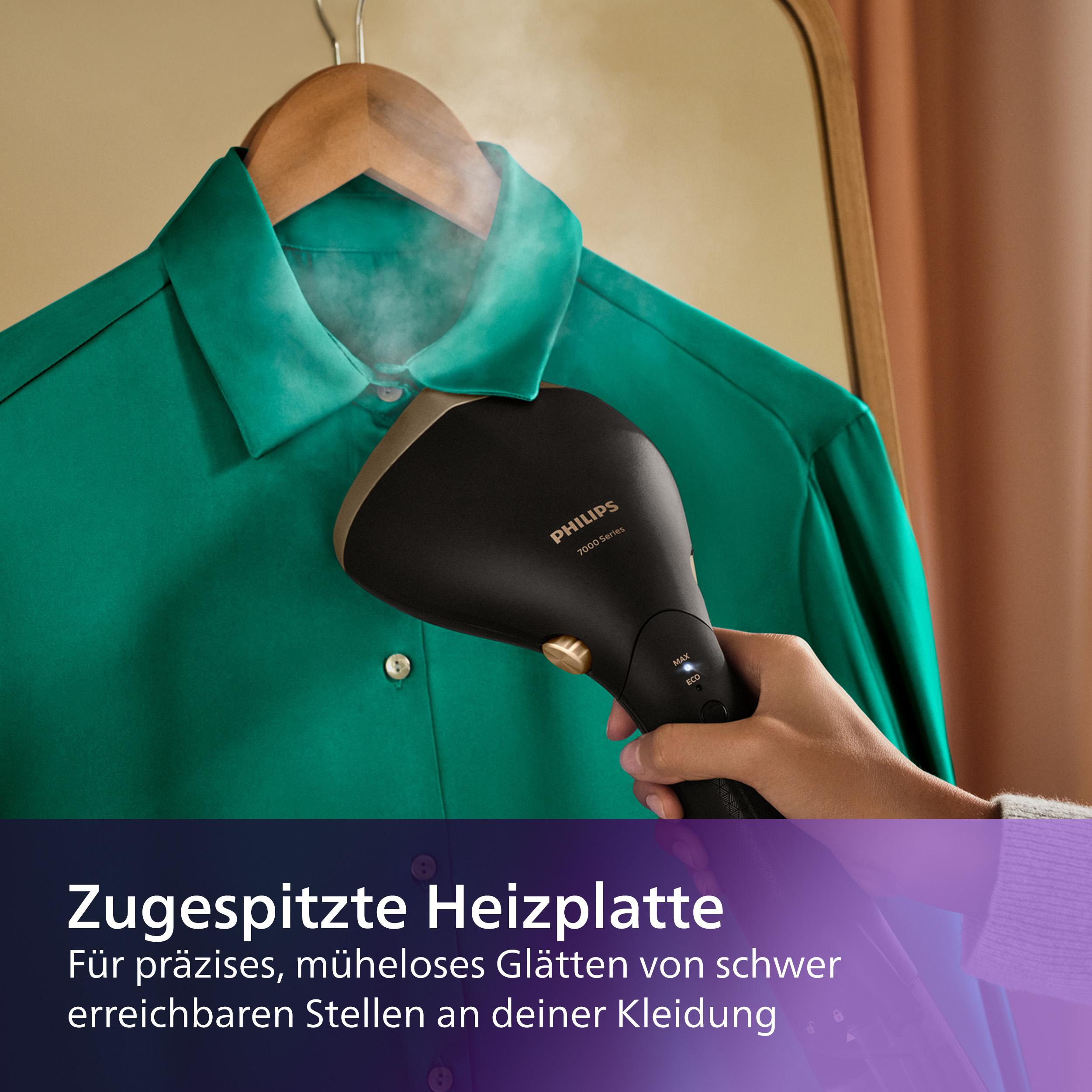 Eine Person dämpft ein grünes Hemd mit einem schwarzen und goldenen Philips-Kleidungsdämpfer. Das Hemd hängt an einem Holzbügel.