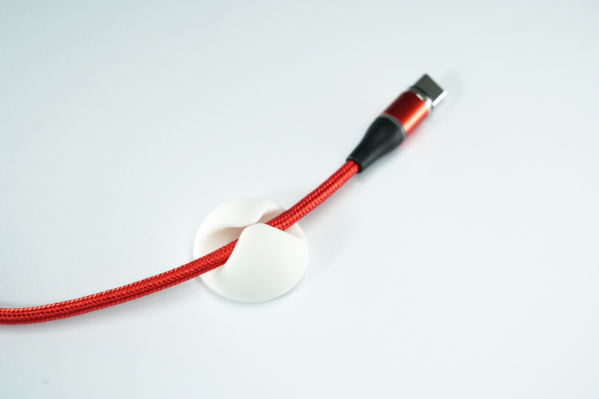 Cavo USB rosso con un organizzatore di cavi bianco, su sfondo bianco.