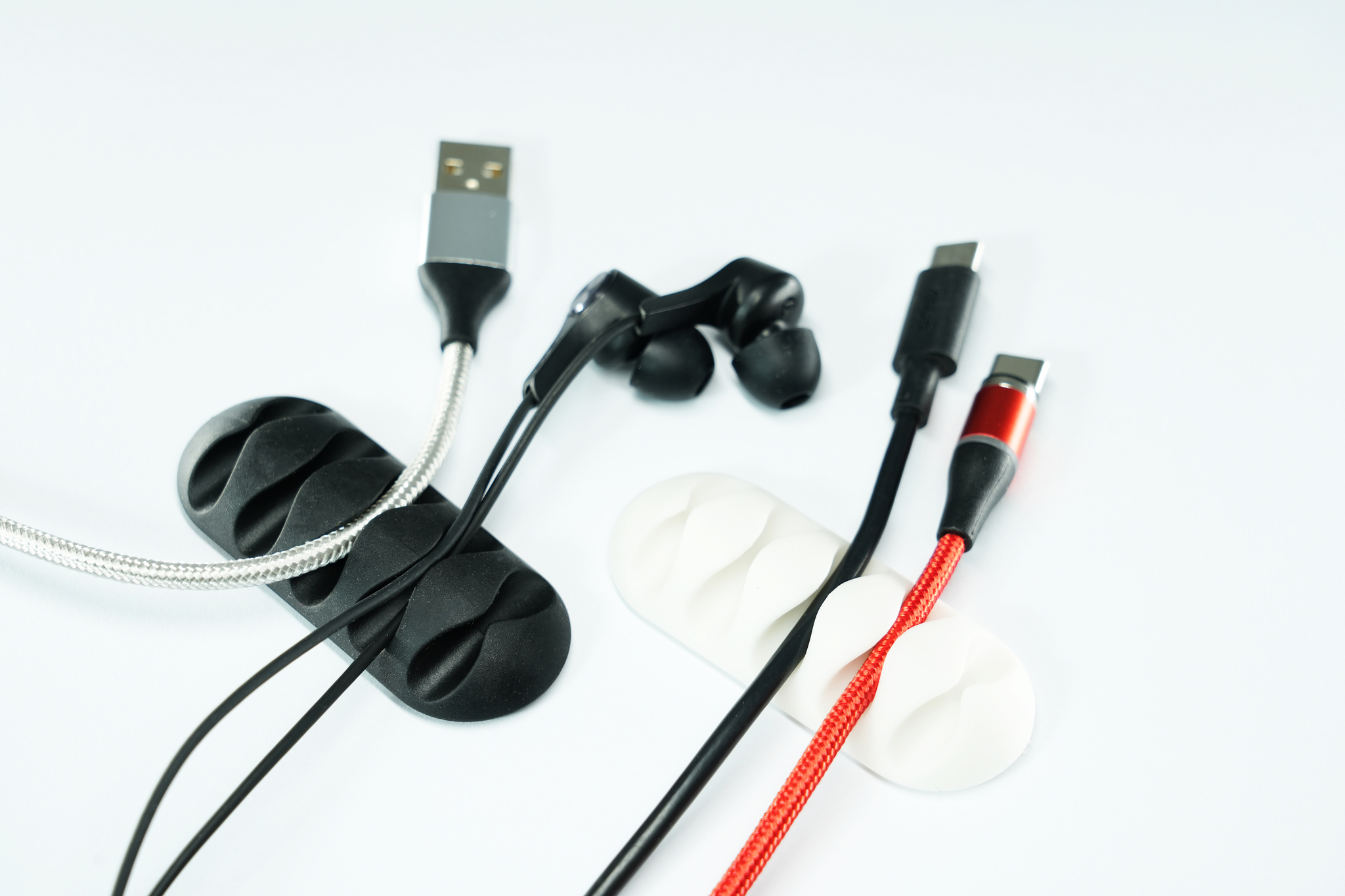 Vari cavi, una USB, auricolari e caricabatterie su una superficie bianca con organizzatori di cavi.