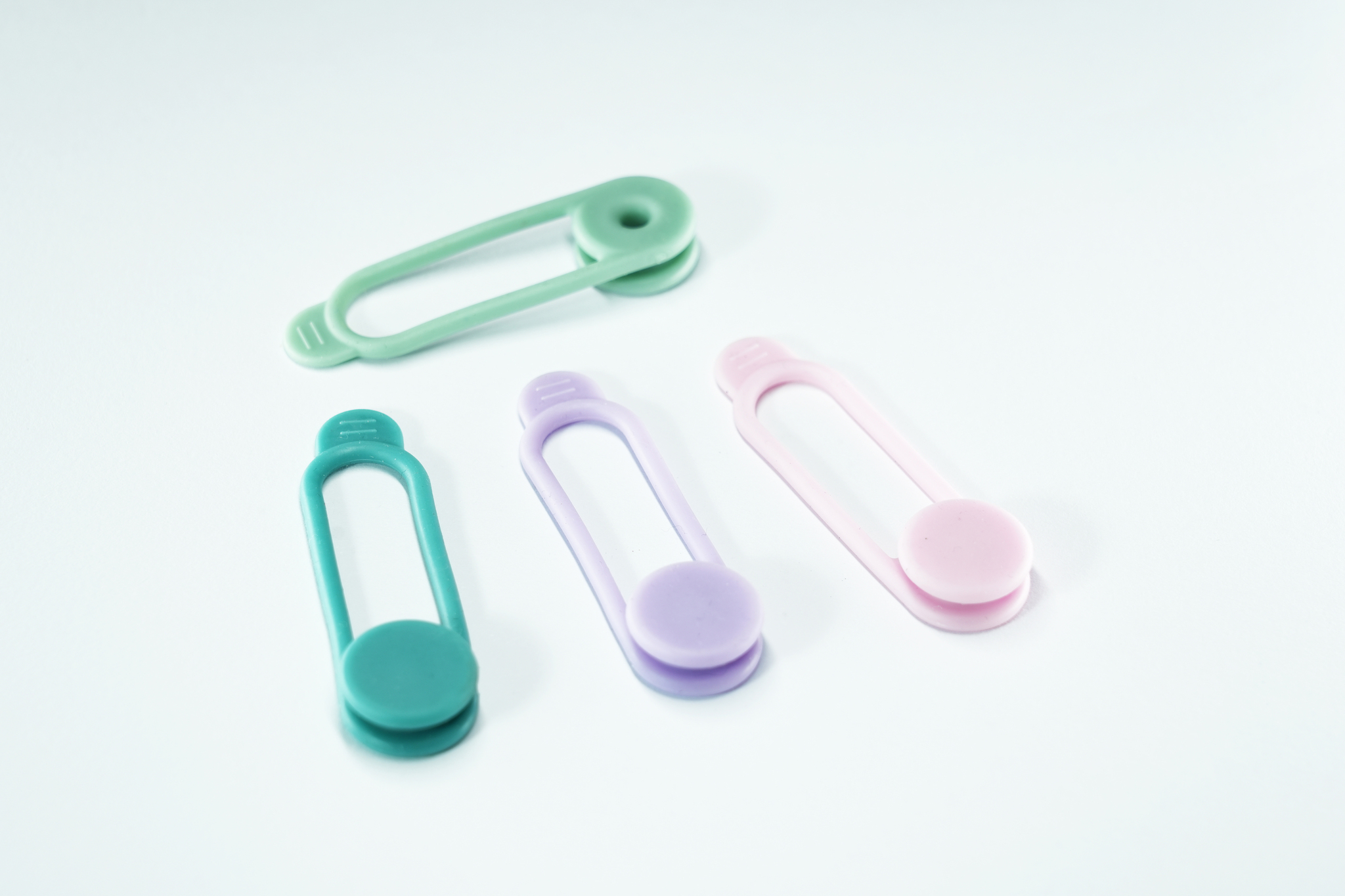 Quattro clip colorati, verde, verde acqua, viola e rosa, disposti su sfondo bianco.