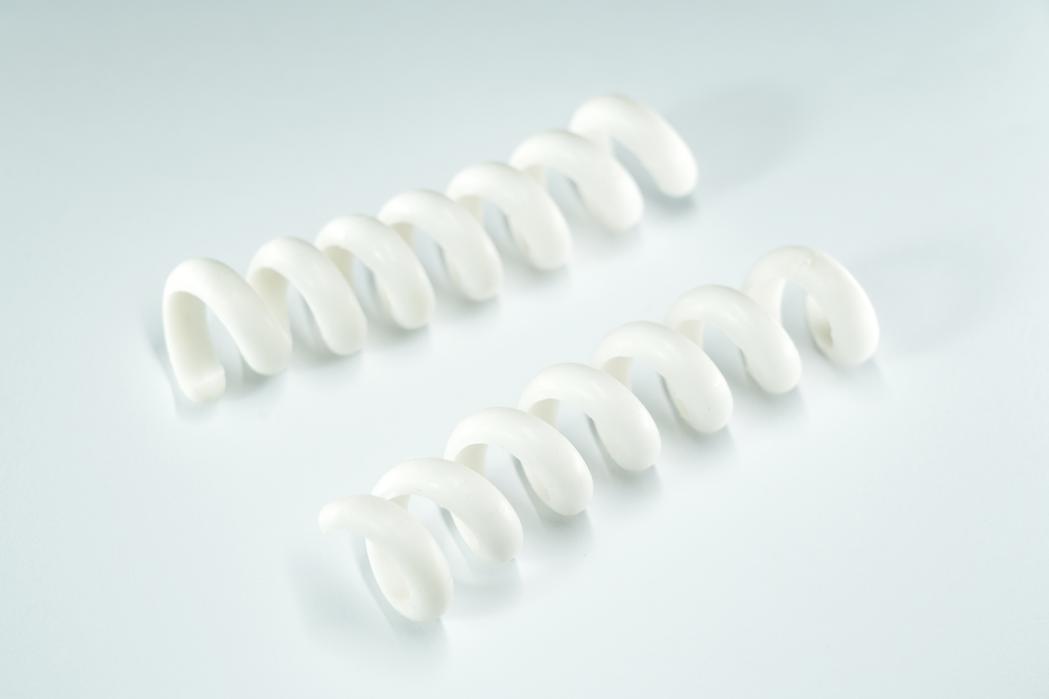 Deux objets en plastique blancs en forme de spirale sur une surface claire.