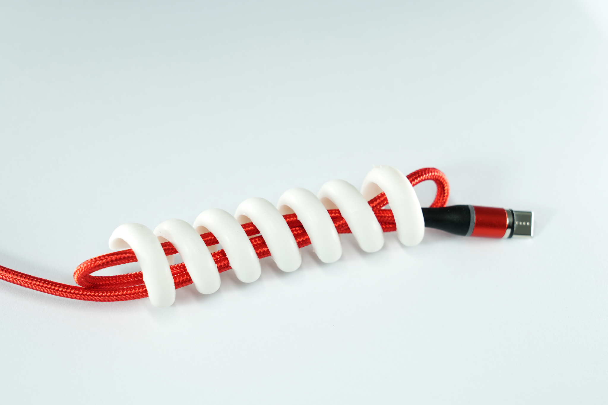 Un câble rouge avec une gaine en spirale blanche. Un connecteur noir et rouge à l'extrémité.
