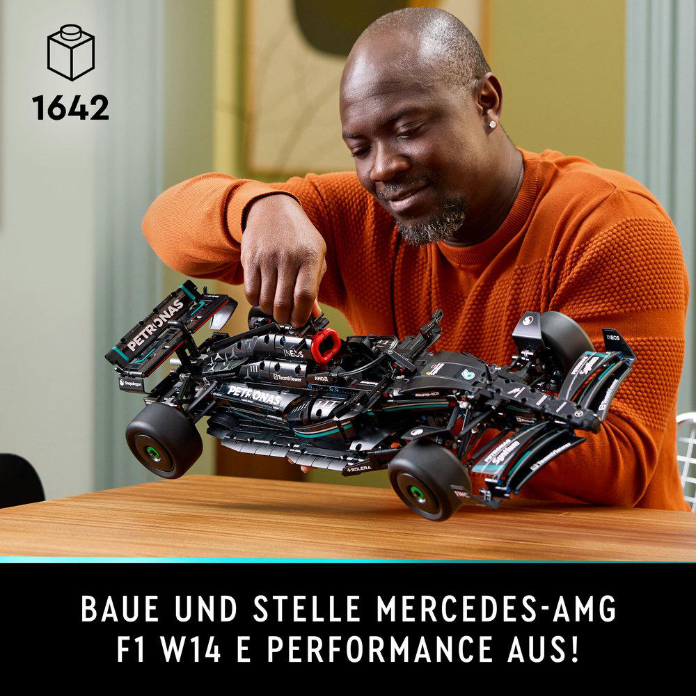 Ein Mann, der ein schwarzes Lego Mercedes-AMG F1-Automodell auf einem Holztisch zusammenbaut und lächelt.