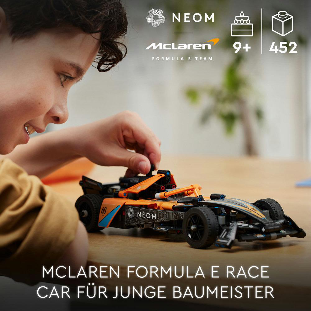 Ein Junge spielt mit einem McLaren-Rennwagenmodell auf einem Holztisch.