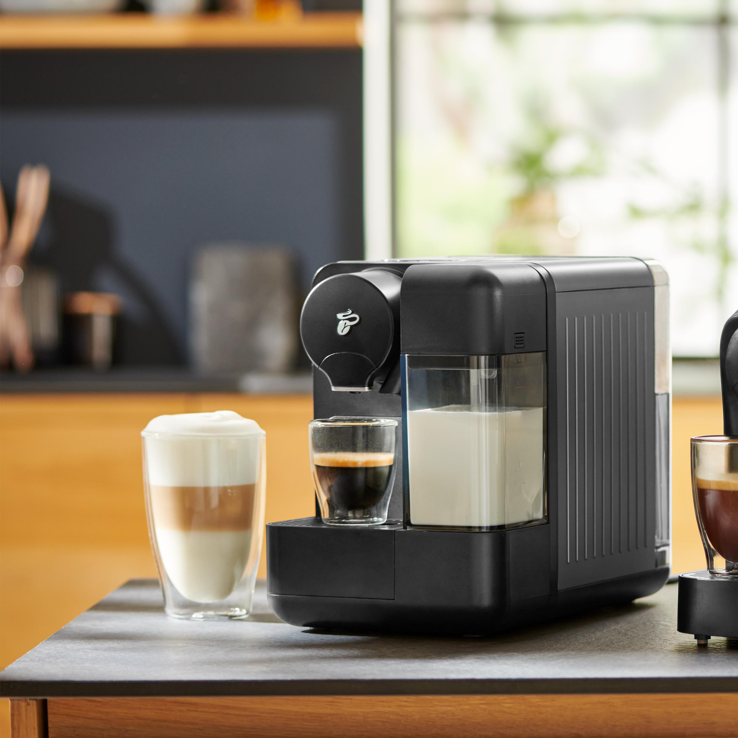 Schwarze Kaffeemaschine mit Kaffee- und Milchgetränken auf einer Theke, mit verschwommenem Hintergrund.