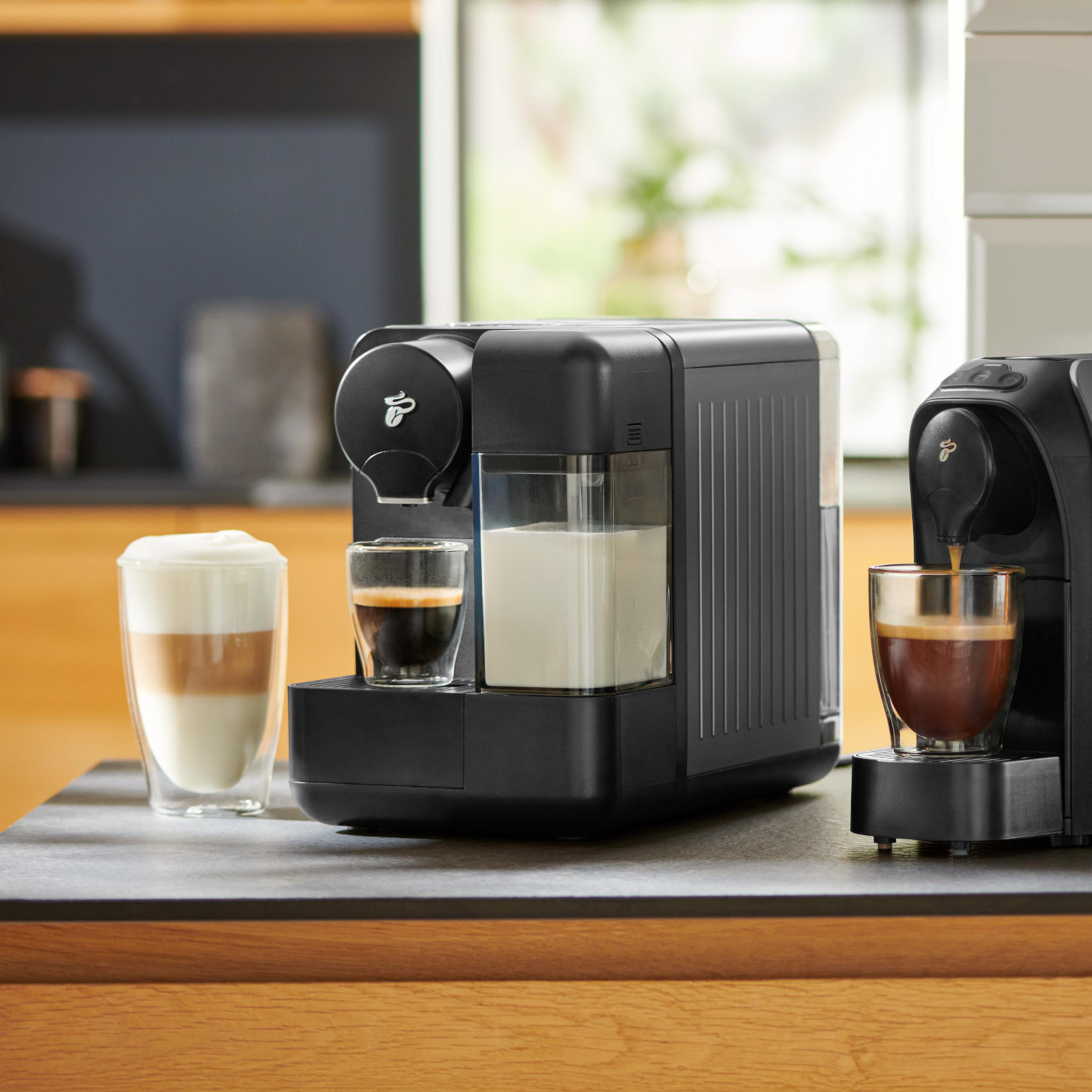 Zwei schwarze Kaffeemaschinen mit verschiedenen Getränken auf einer Arbeitsplatte.