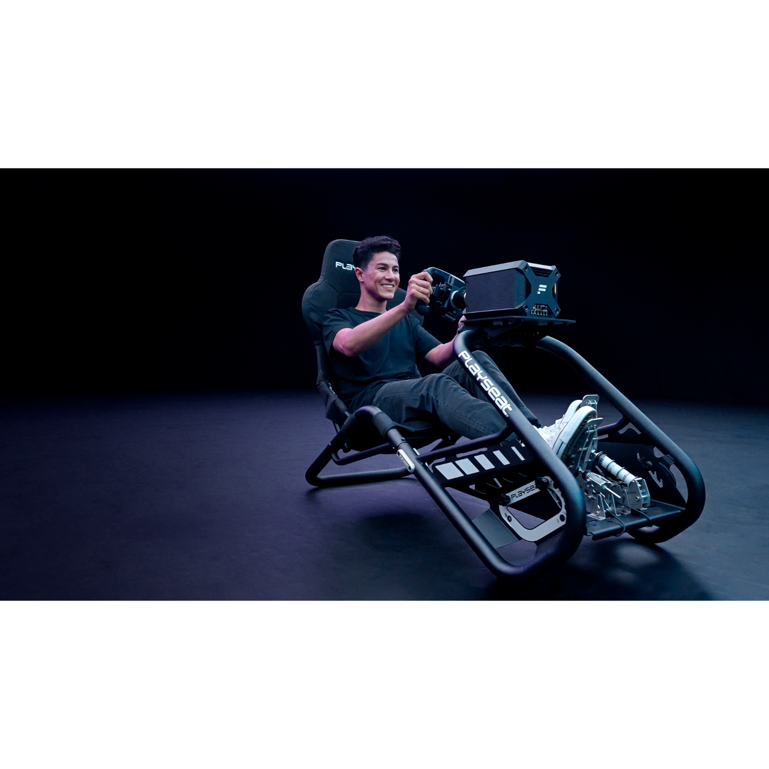 Een man in een racesimulator met een stuur, lachend, in een donkere omgeving.
