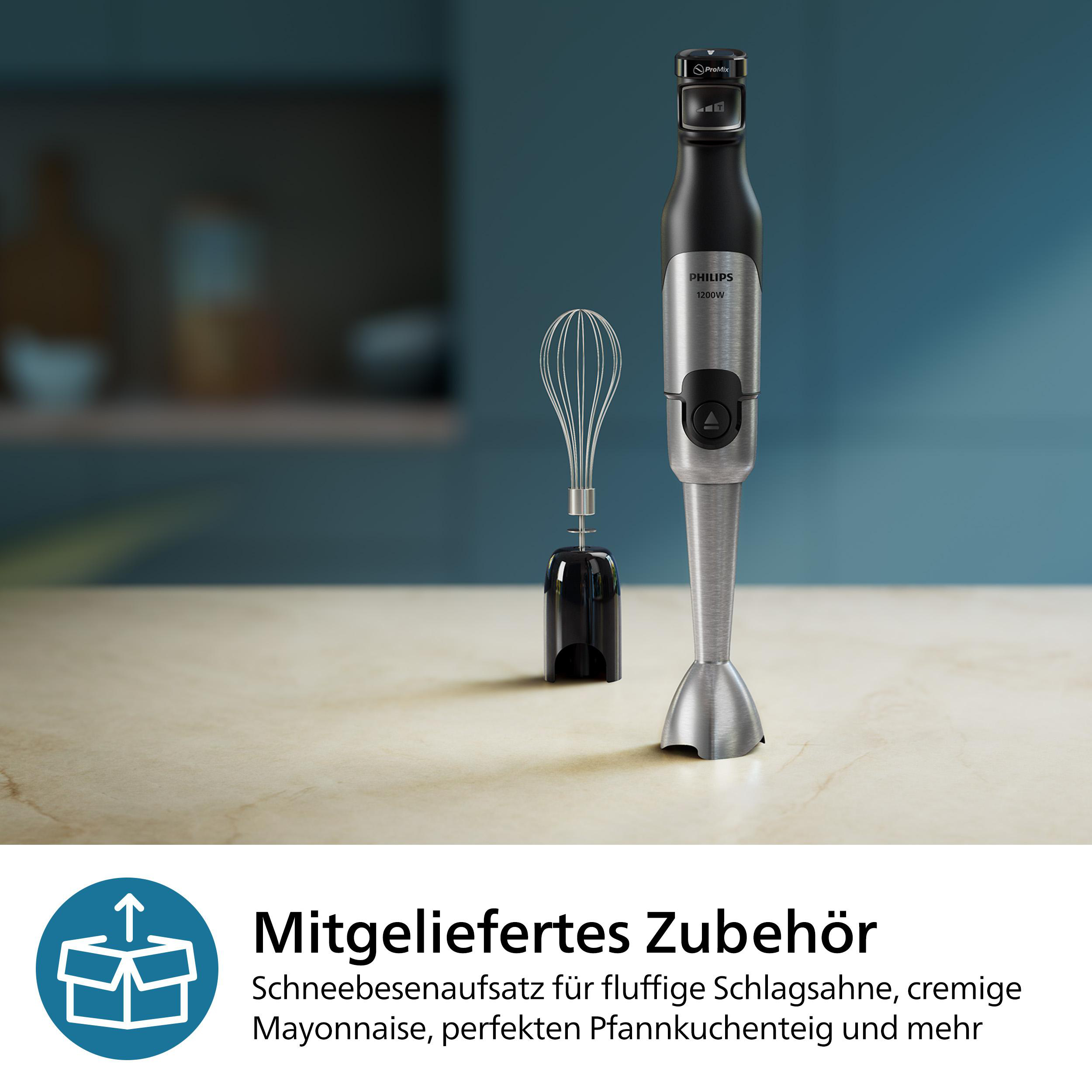 Ein Stabmixer mit Zubehör. Er ist silber und schwarz, platziert auf einem hellen Tisch.