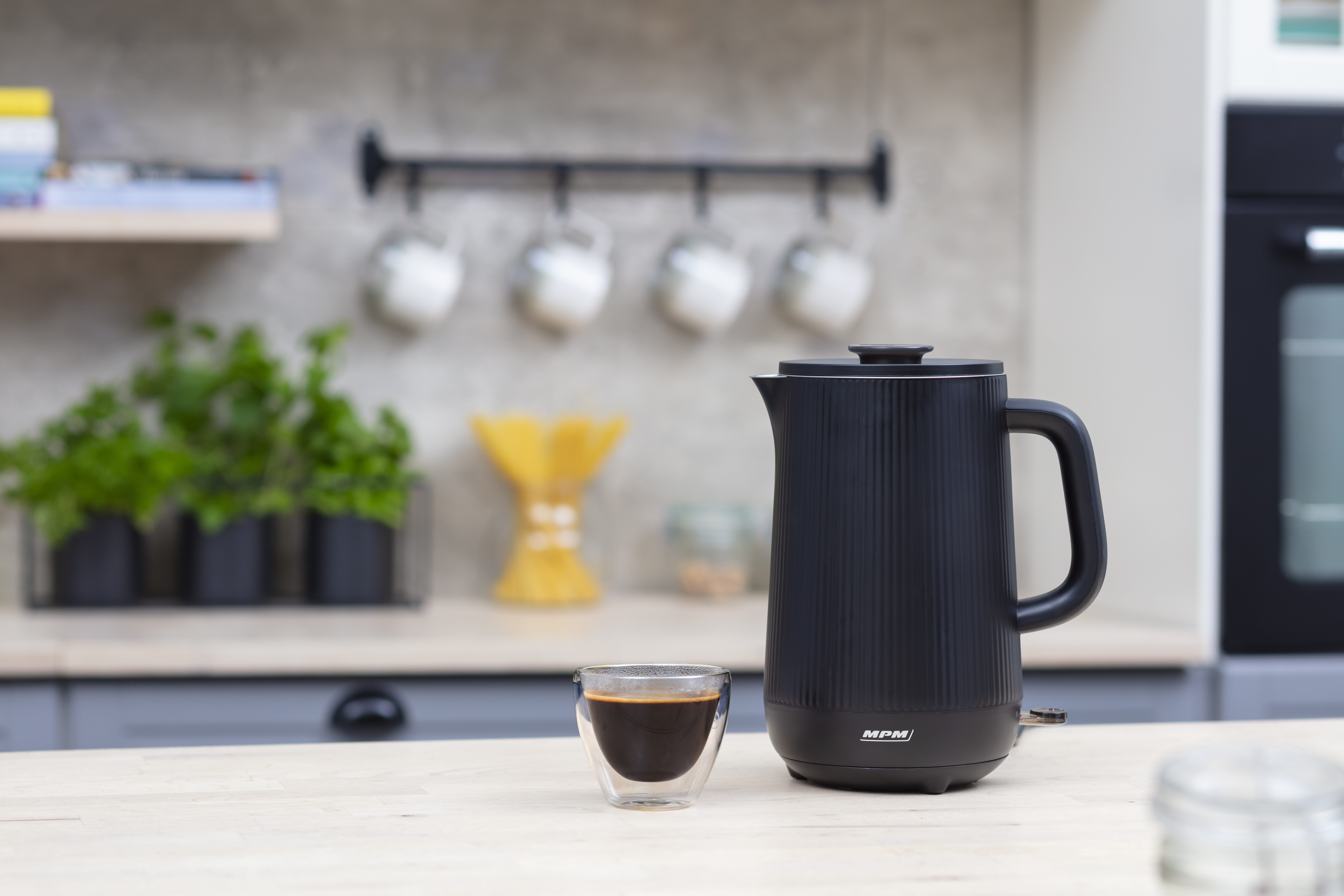 Czarny czajnik elektryczny i szklanka kawy na drewnianej powierzchni w kuchni.