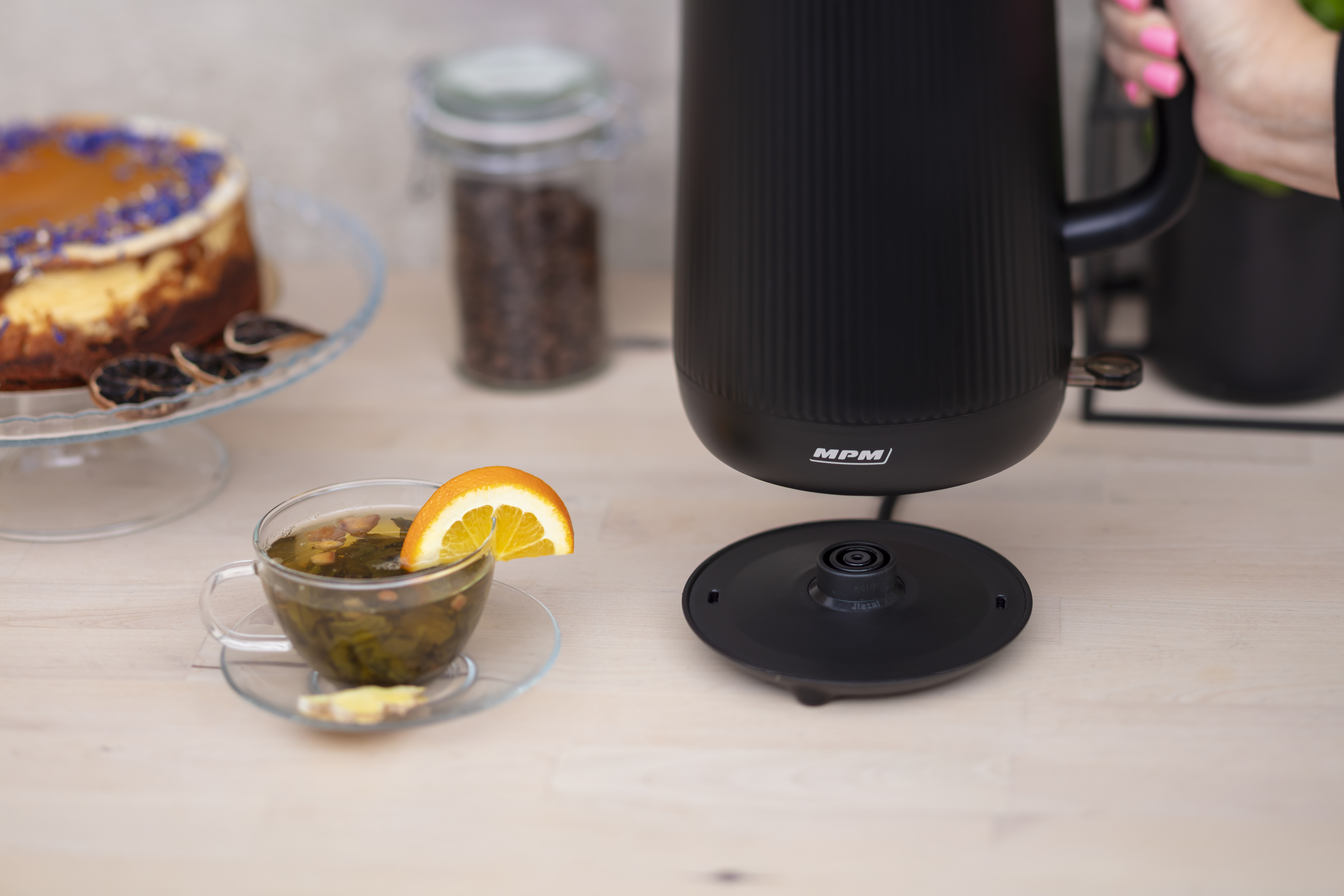 Czarny czajnik elektryczny z filiżanką herbaty i plasterkiem pomarańczy. Rozmyte tło.