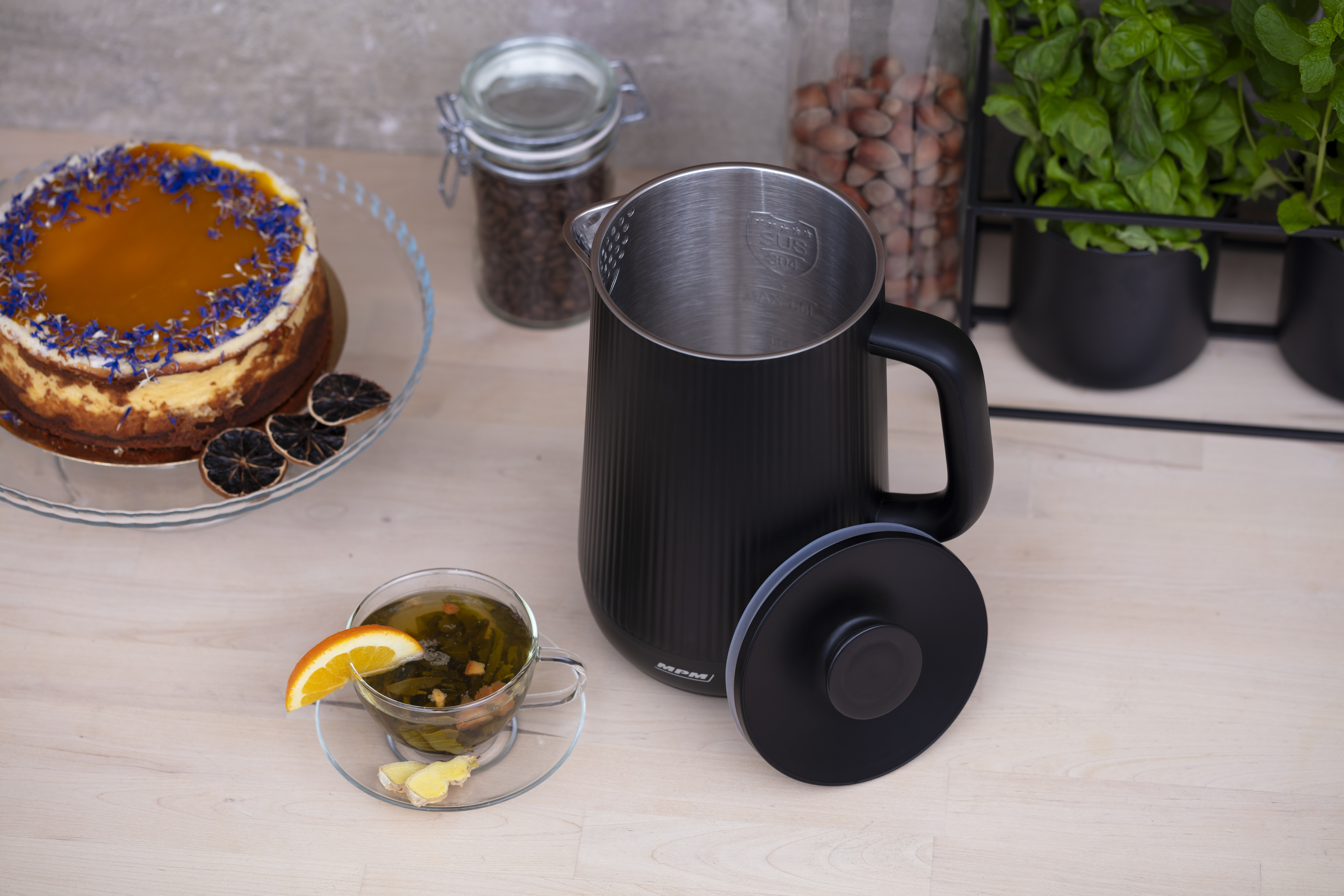 Czajnik w kolorze czarnym z filiżanką herbaty, ciastem i innymi akcesoriami kuchennymi.