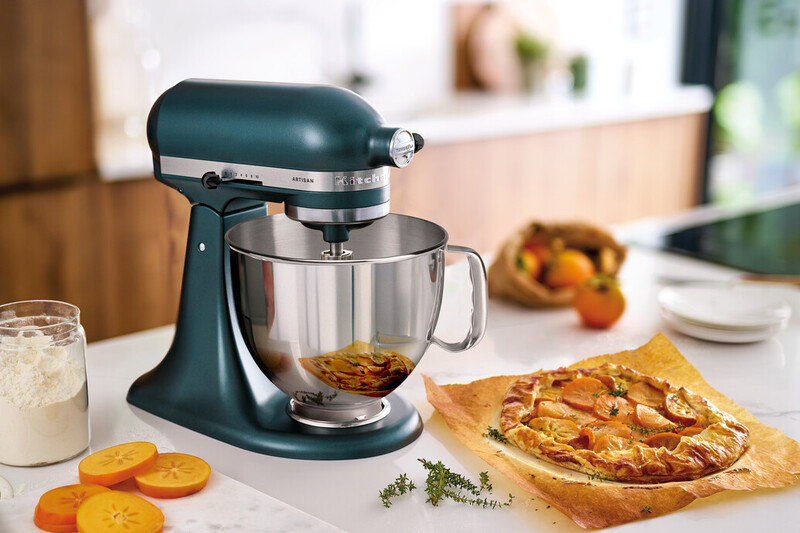Ein türkisfarbener KitchenAid-Küchenmixer mit Schüssel, in der Nähe einer Galette und Kaki-Scheiben.