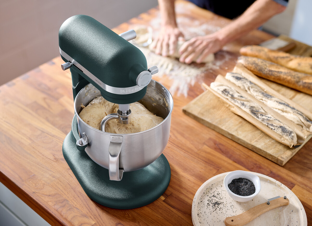 Eine türkisfarbene KitchenAid-K üchenmaschine verrührt Teig. Hände einer Person im Hintergrund kneten Teig.