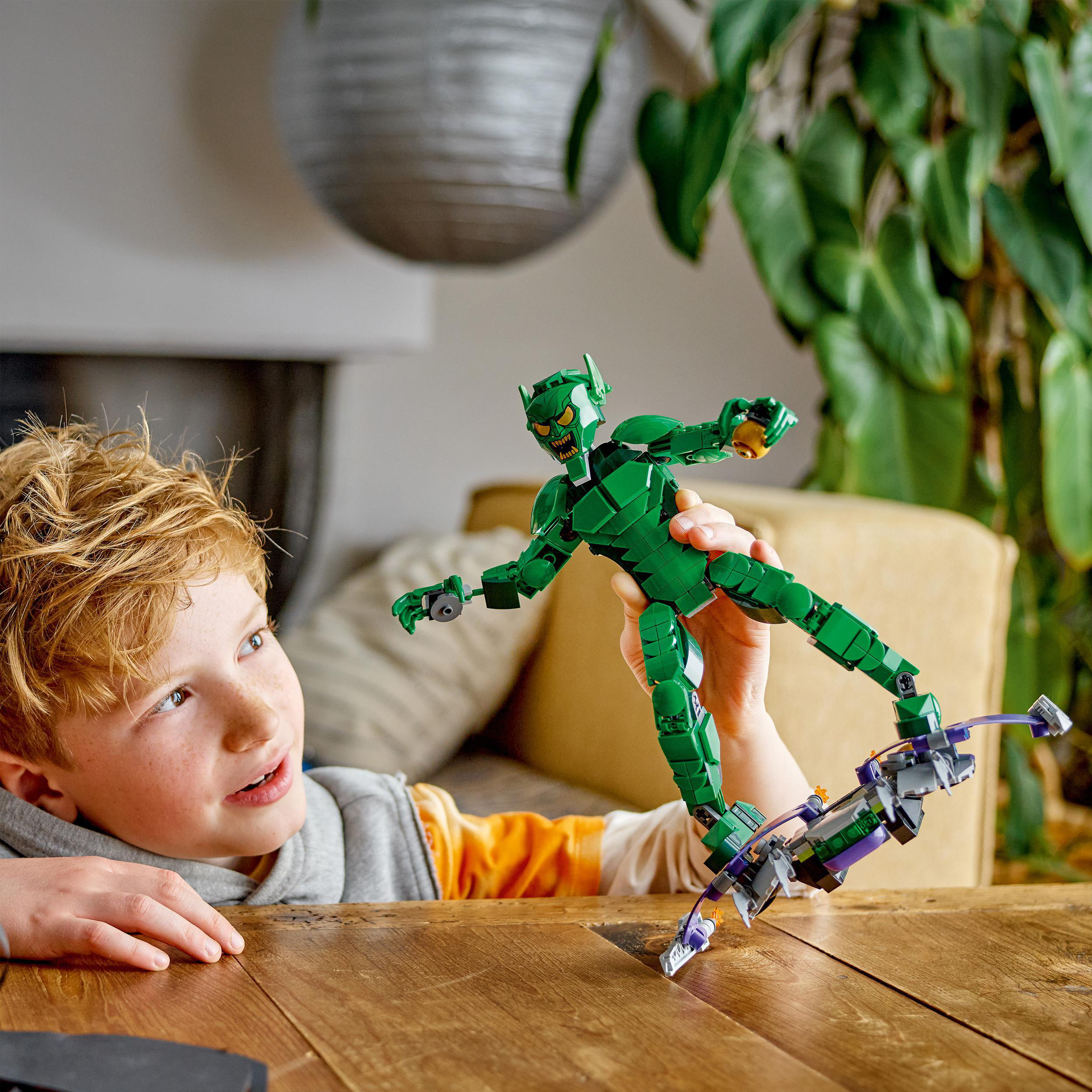 Ein Junge betrachtet eine Lego-Figur des Green Goblin. Der Junge hält die Figur. Eine Pflanze ist im Hintergrund.
