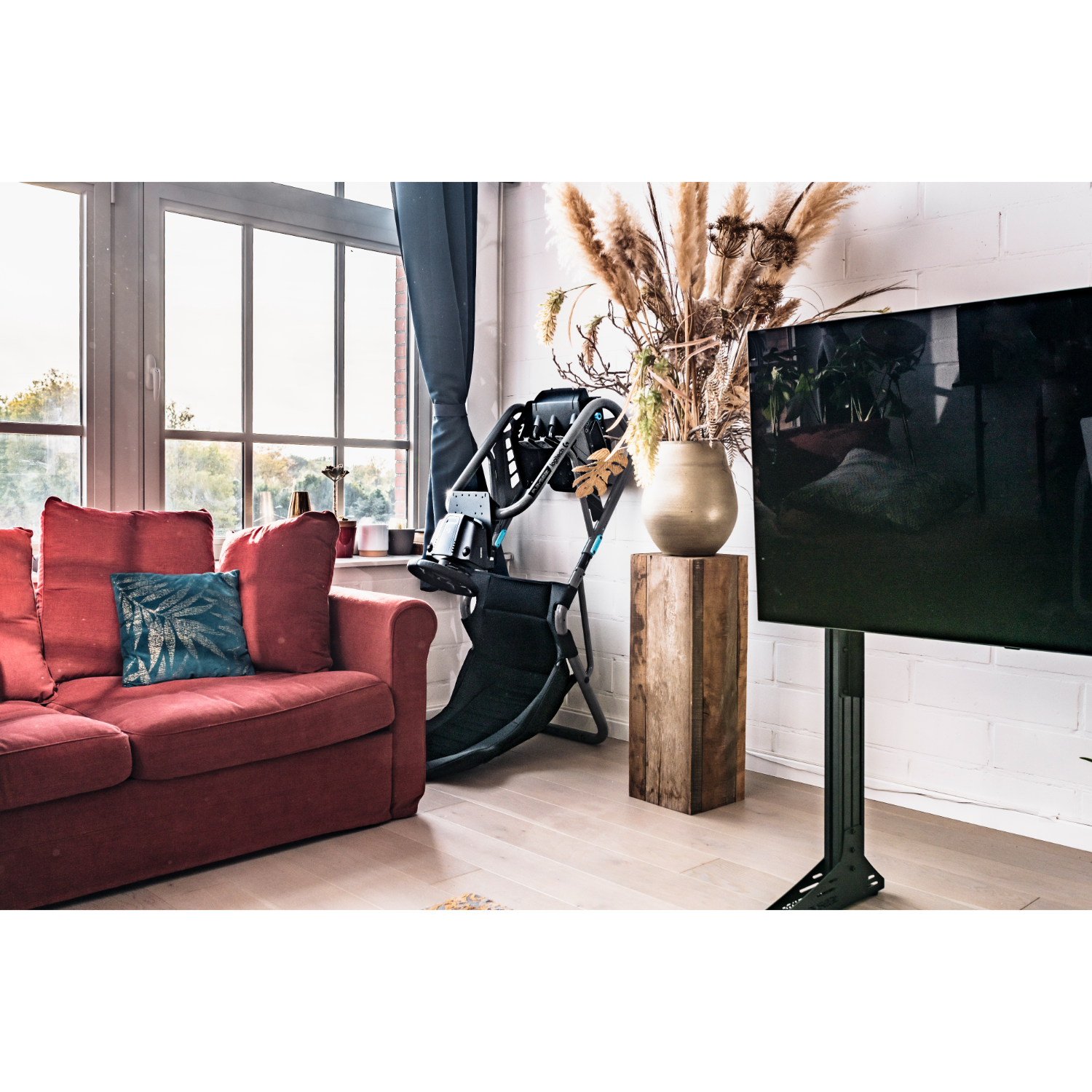 Living room with a red sofa, a TV on a stand, a window, and a wooden stool with plants.