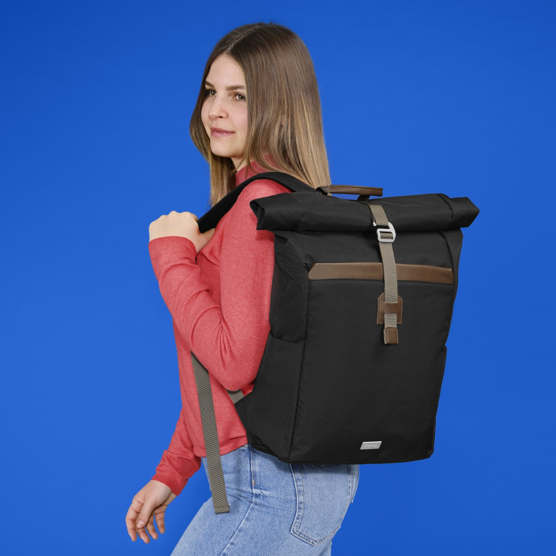 Eine Frau mit Rucksack vor blauem Hintergrund. Sie blickt nach links.