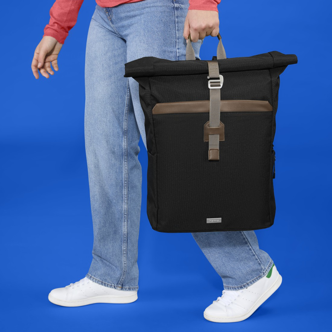 Person geht mit einem schwarzen Rucksack. Der Rucksack ist aufgerollt. Person trägt Jeans und ein rotes Hemd.