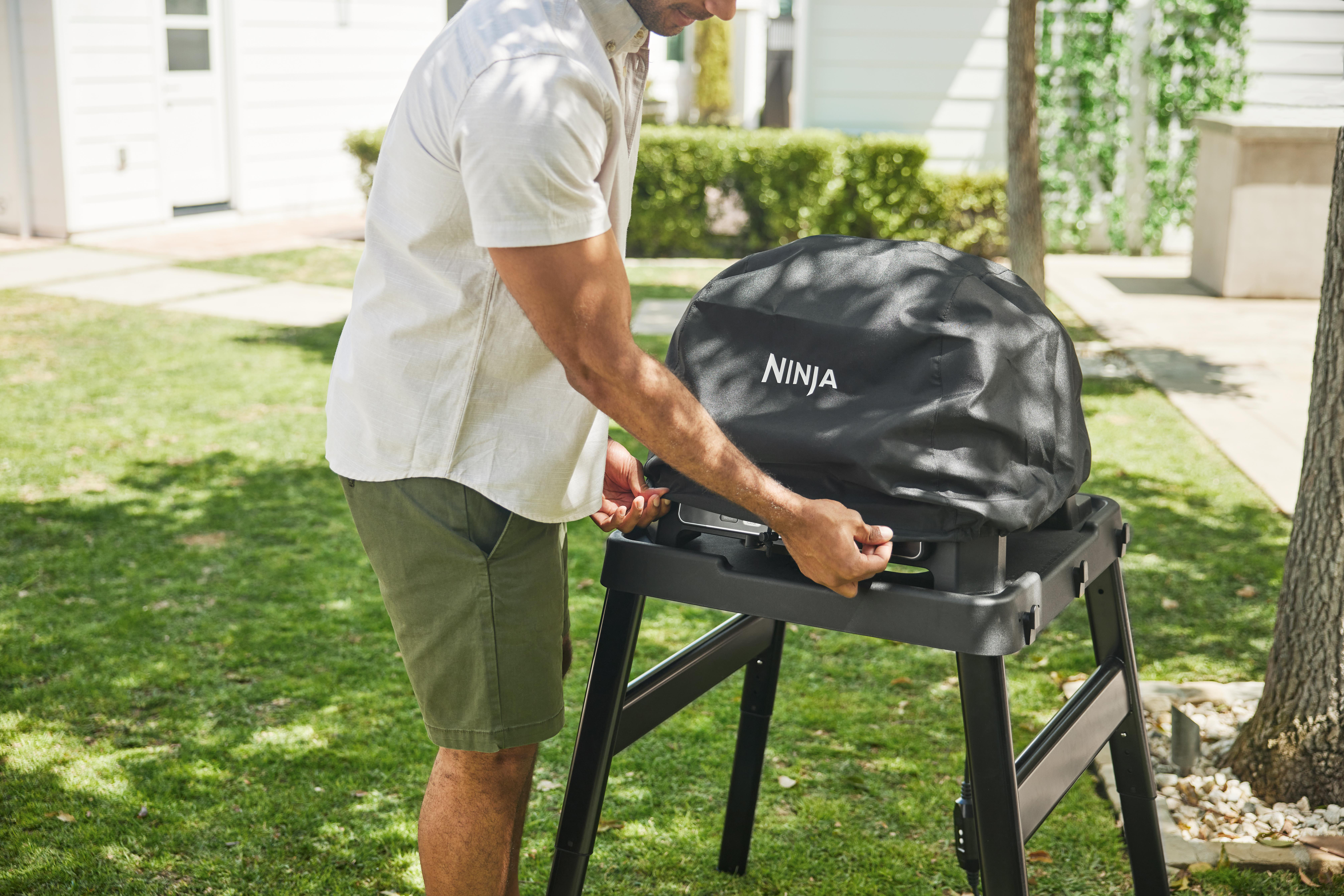 Mann in Shorts legt Abdeckung auf schwarzen Grill im Gras.
